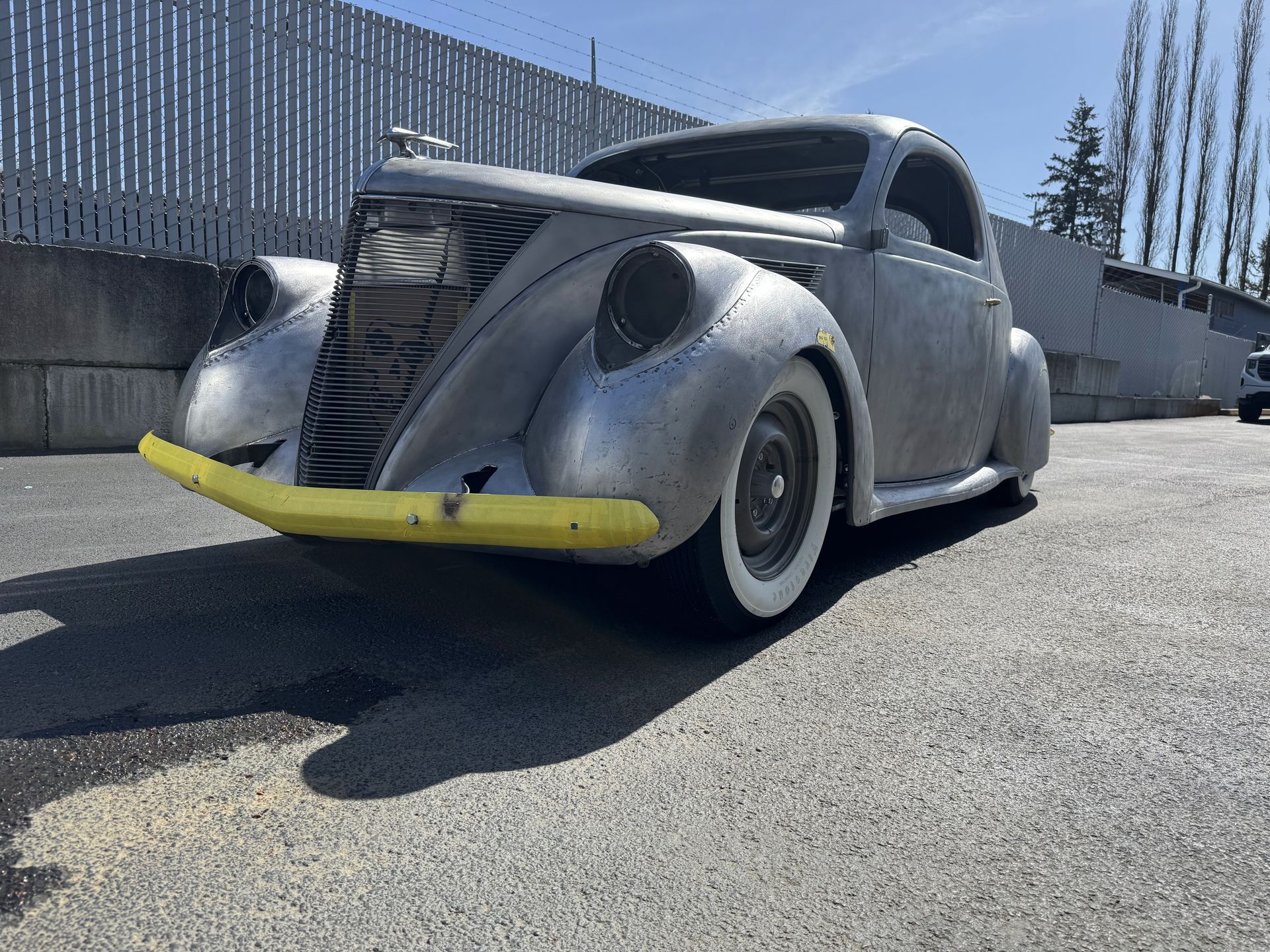 A silver car with a yellow bumper is parked in a parking lot.