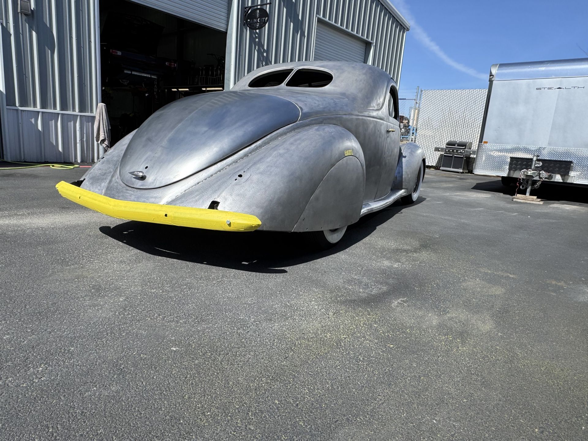A silver car with a yellow bumper is parked in front of a building.