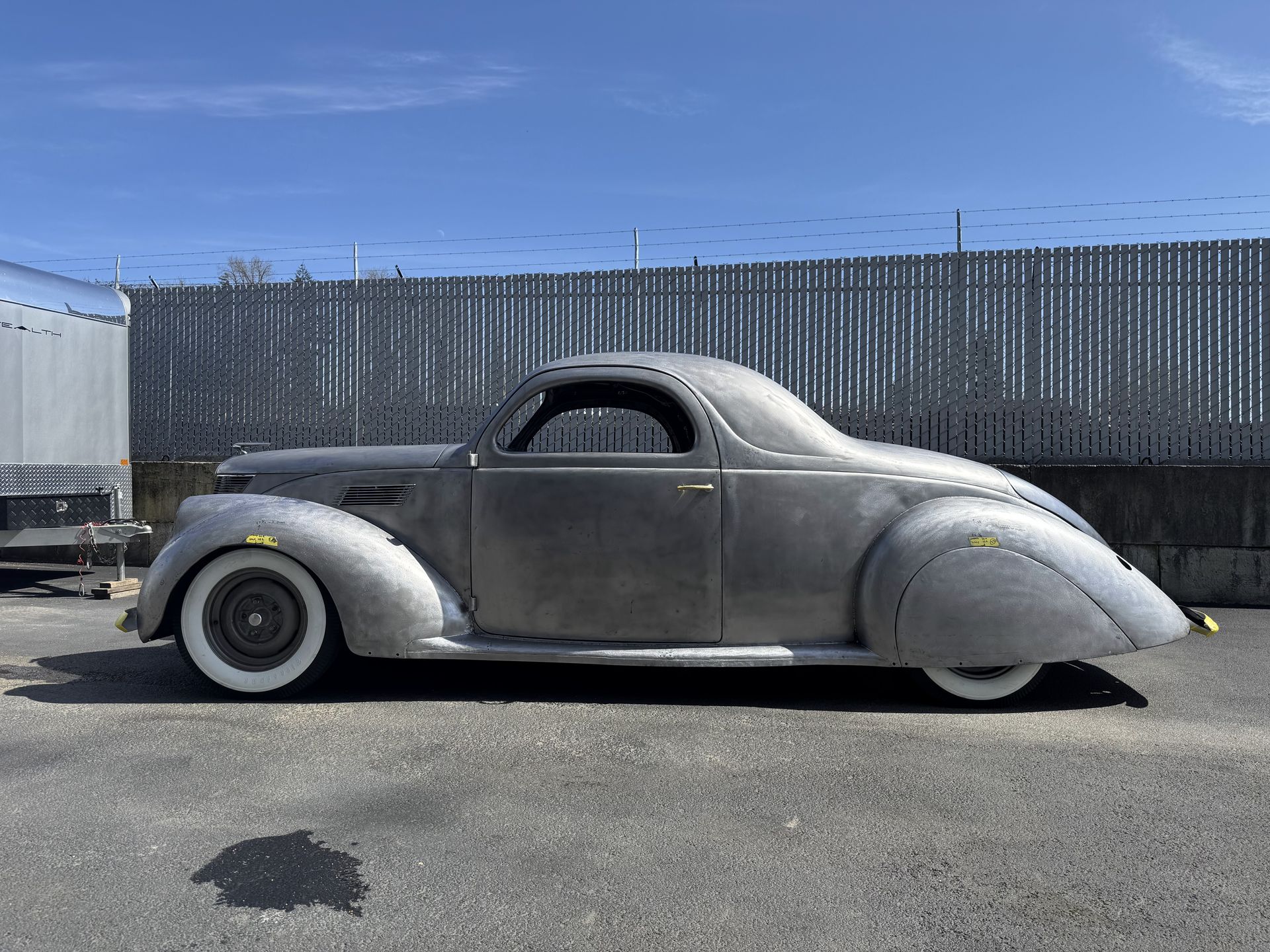 A silver car is parked in a parking lot next to a fence.