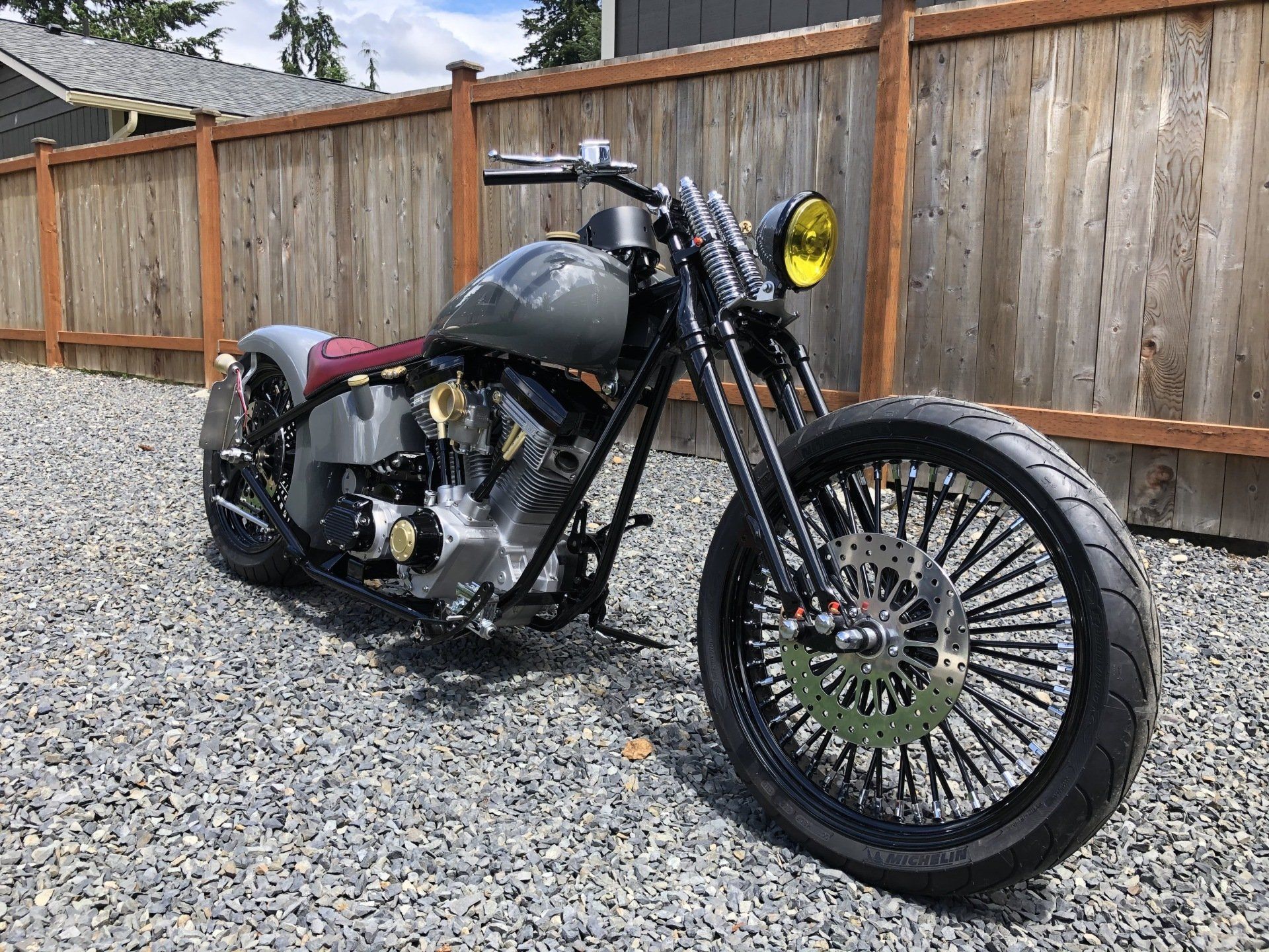 A motorcycle is parked in a gravel lot in front of a wooden fence.