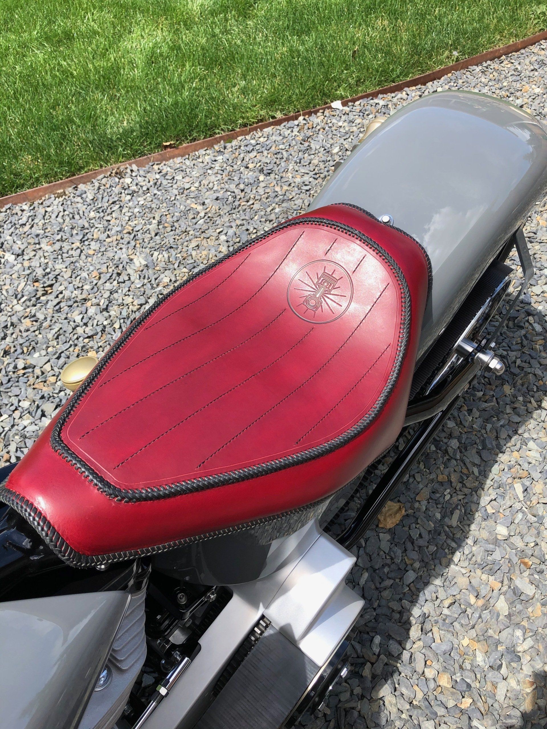 A motorcycle with a red seat is parked on gravel.