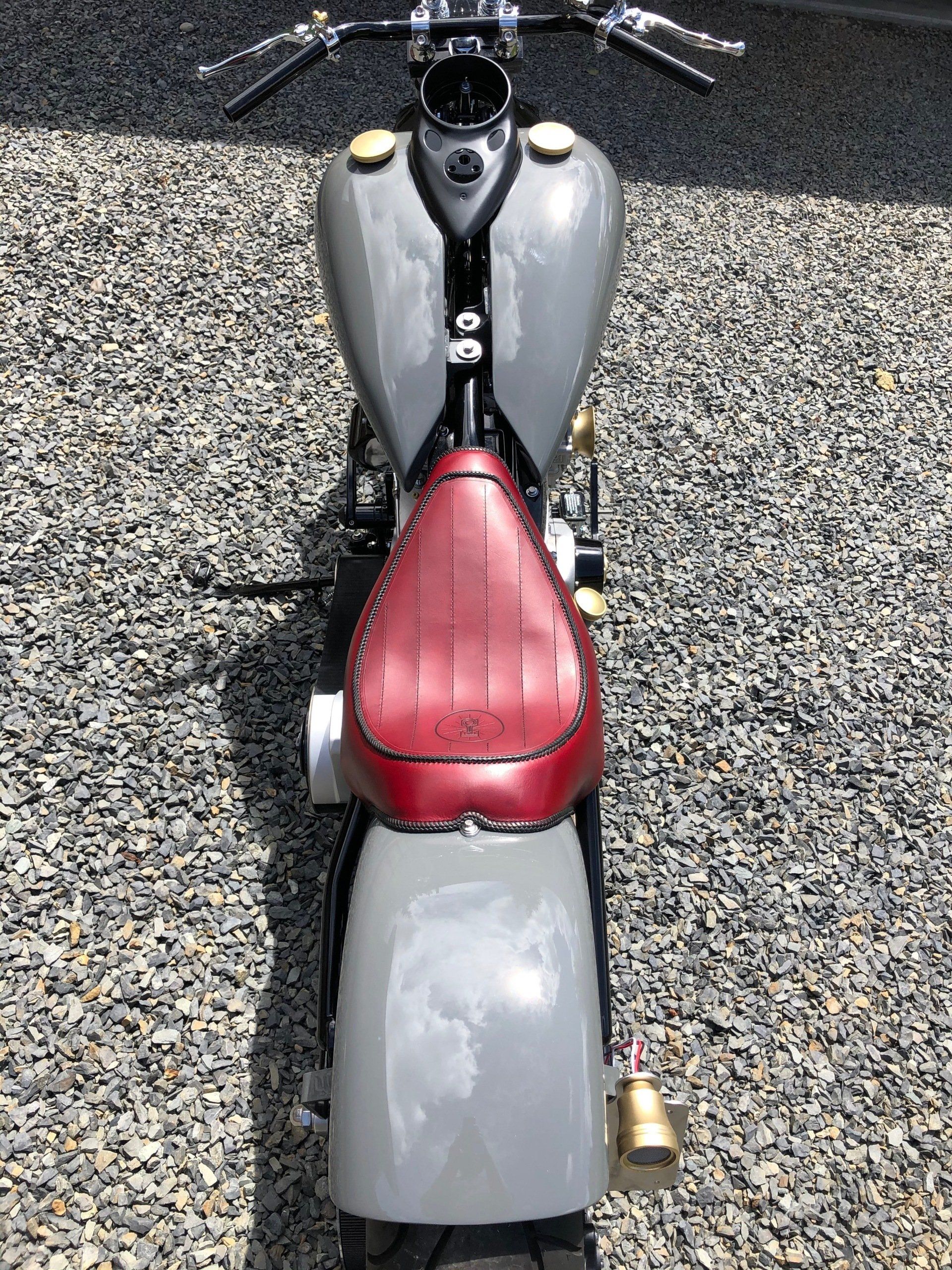 A motorcycle with a red seat is parked on gravel.