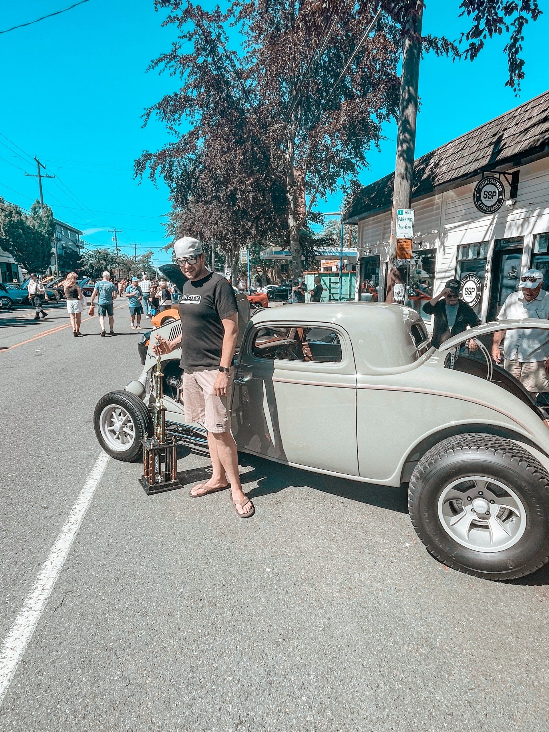 A man is standing next to a vintage car on the side of the road.