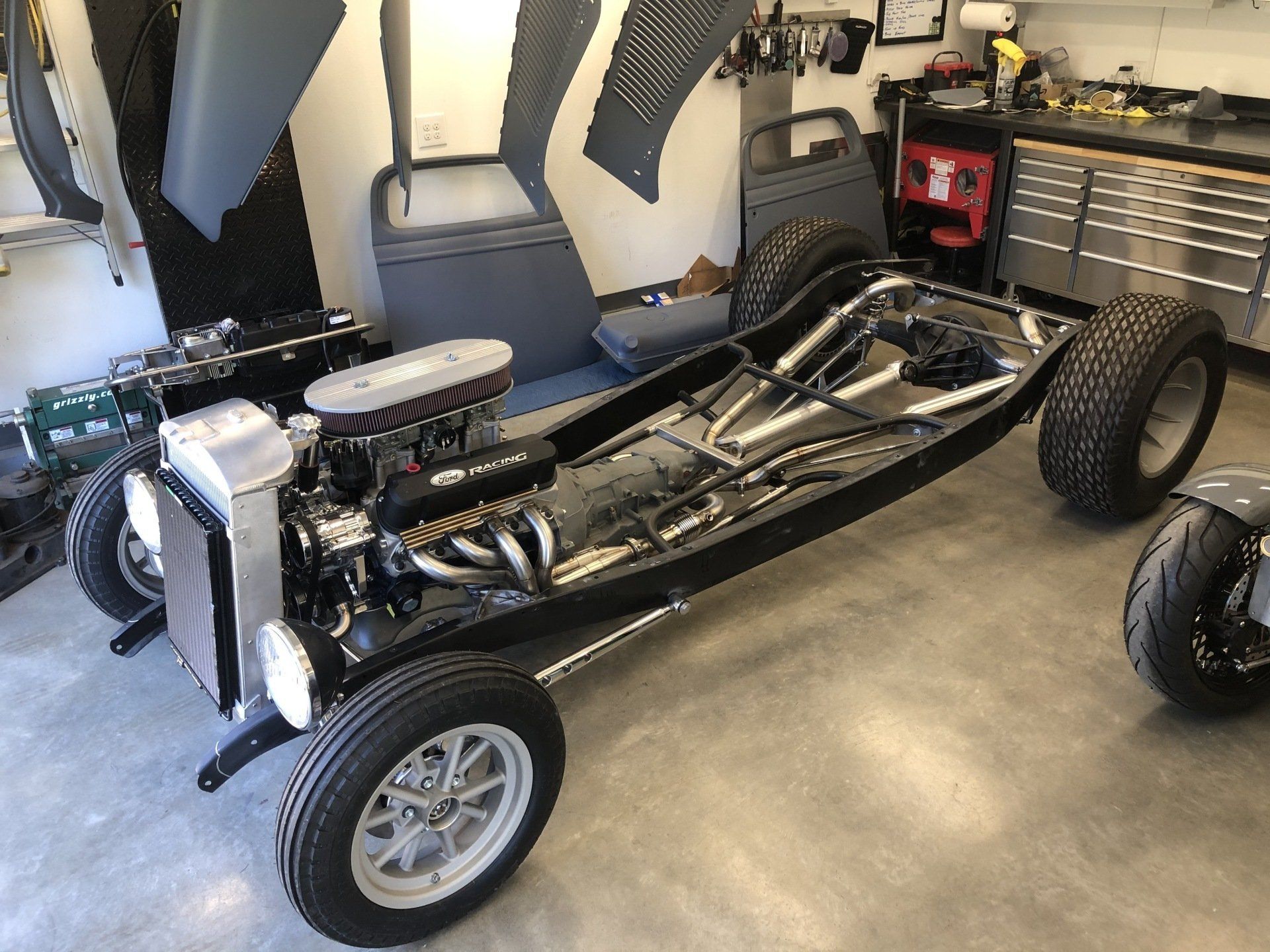A car frame is sitting in a garage next to a motorcycle.