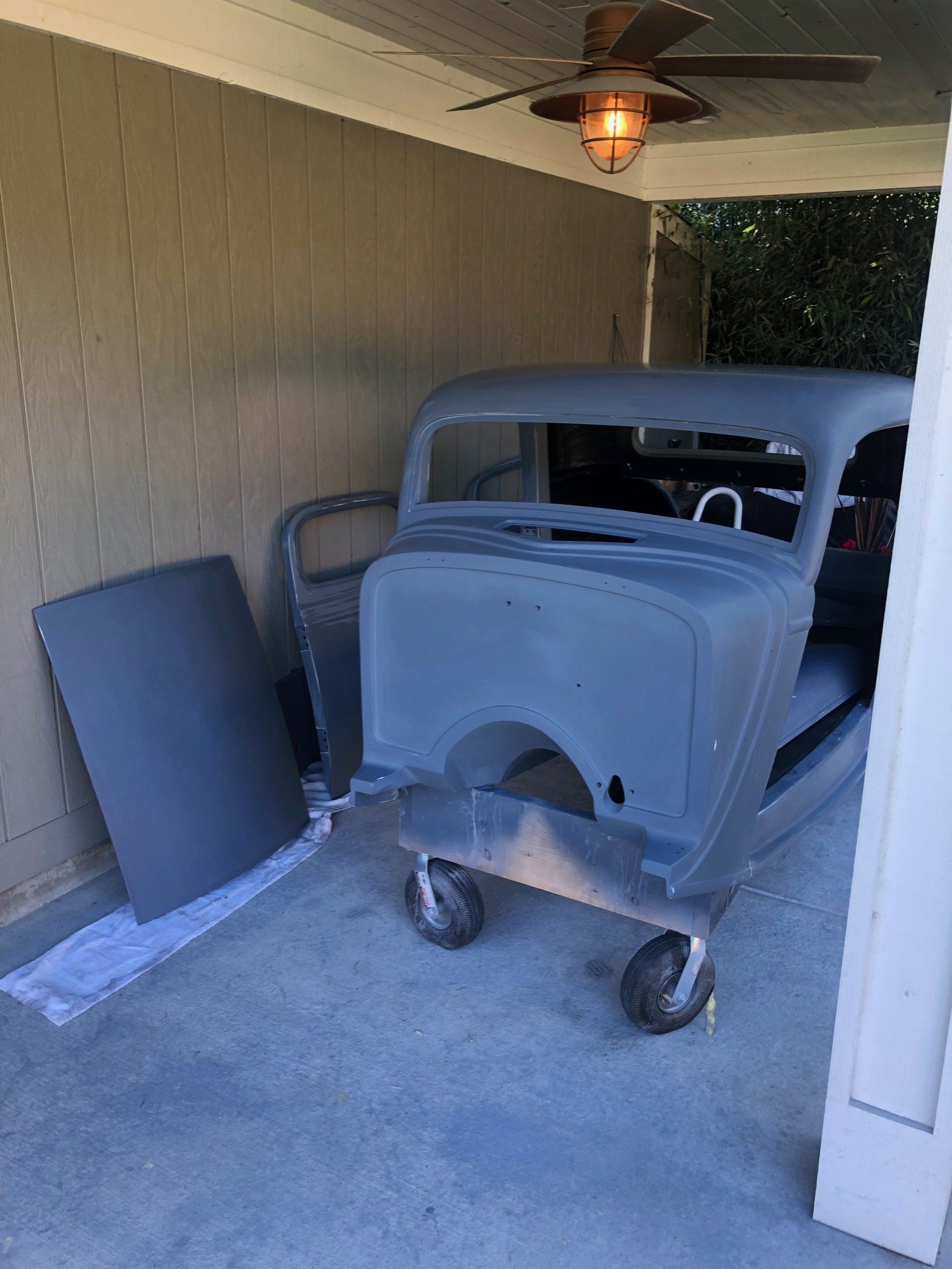 A car is sitting on a cart under a ceiling fan in a garage.