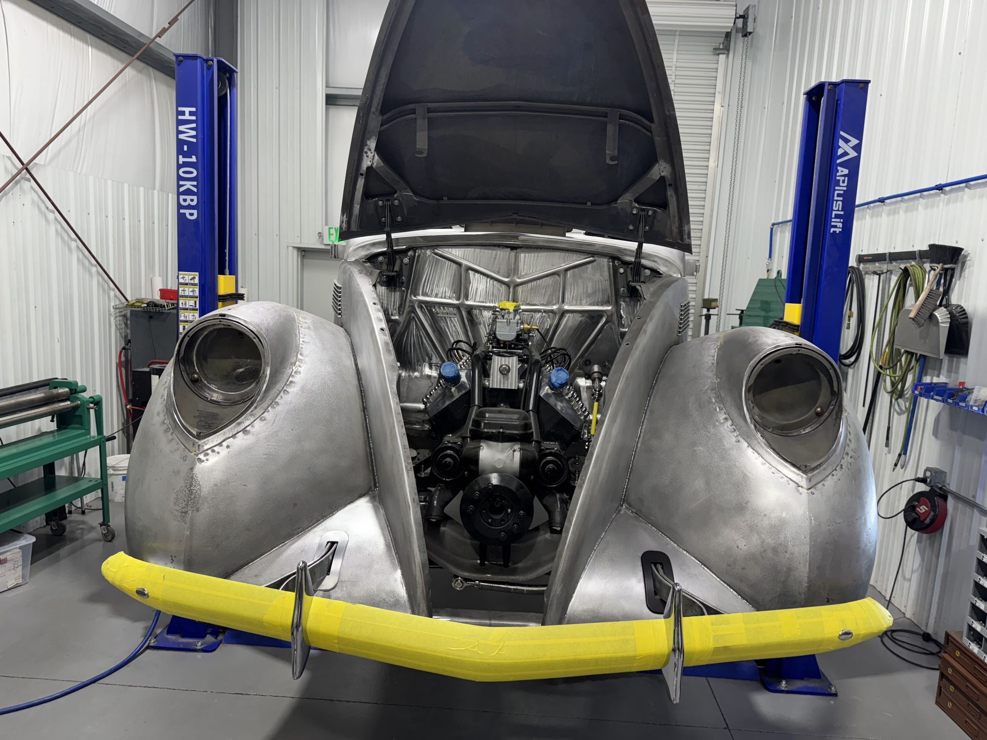 A car with the hood up is sitting on a lift in a garage.