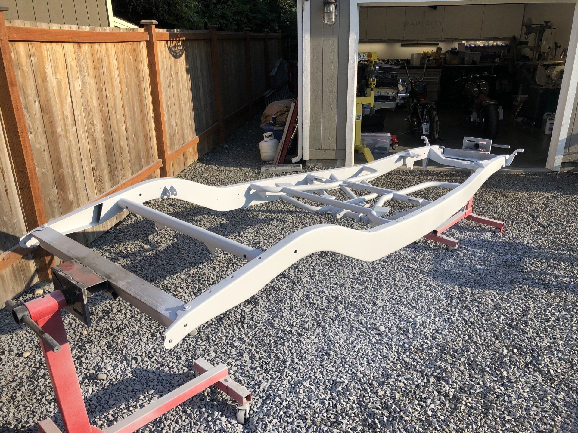 A white metal frame is sitting on gravel in front of a garage.