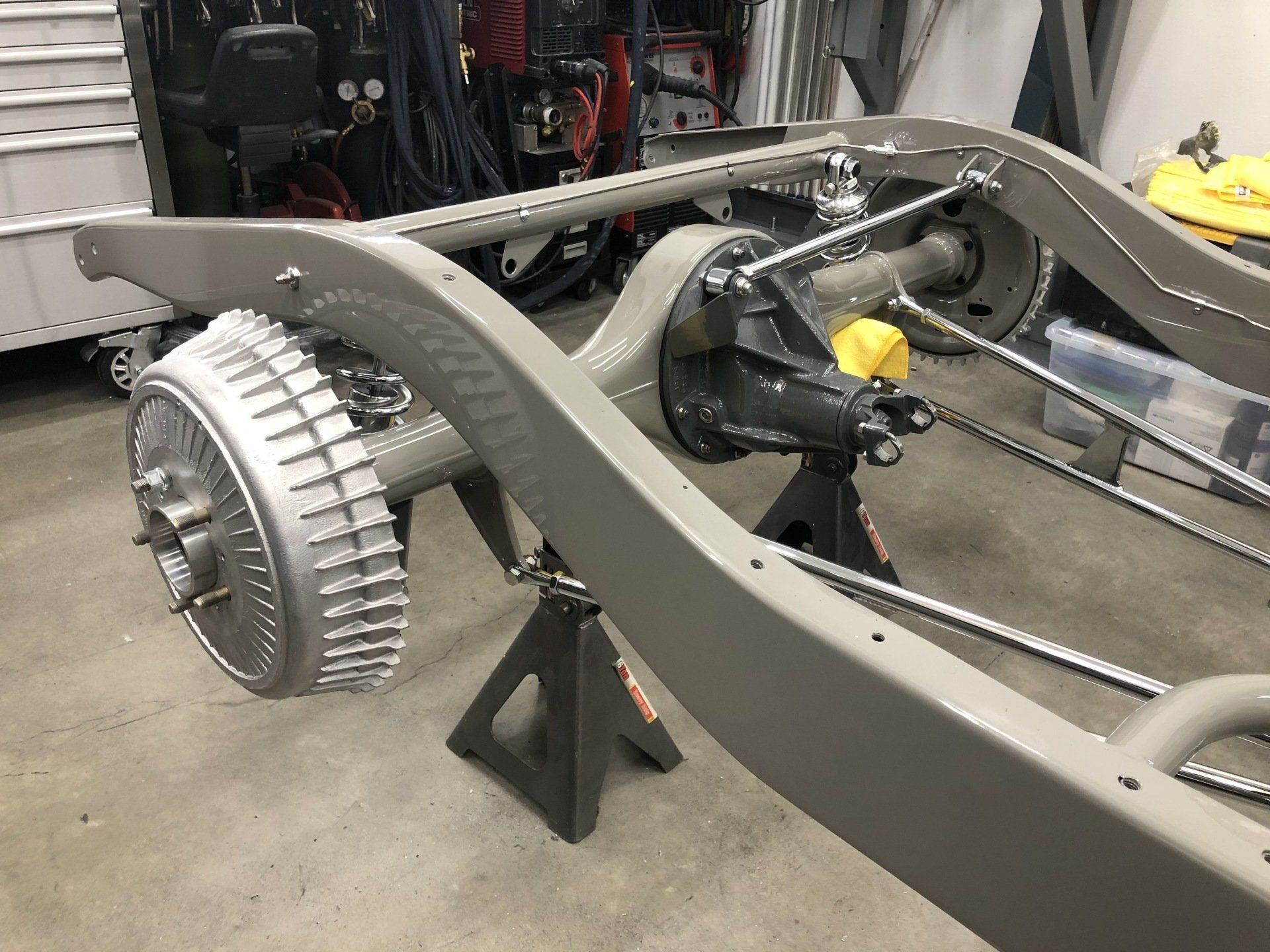 A car chassis is sitting on a jack stand in a garage.