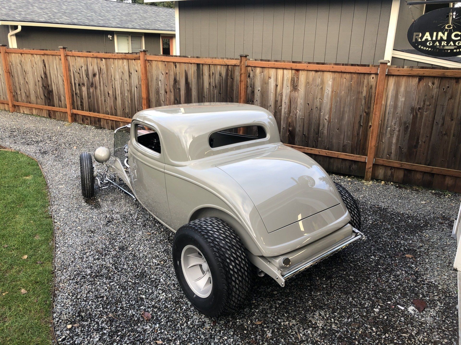 An old car is parked in front of a wooden fence.