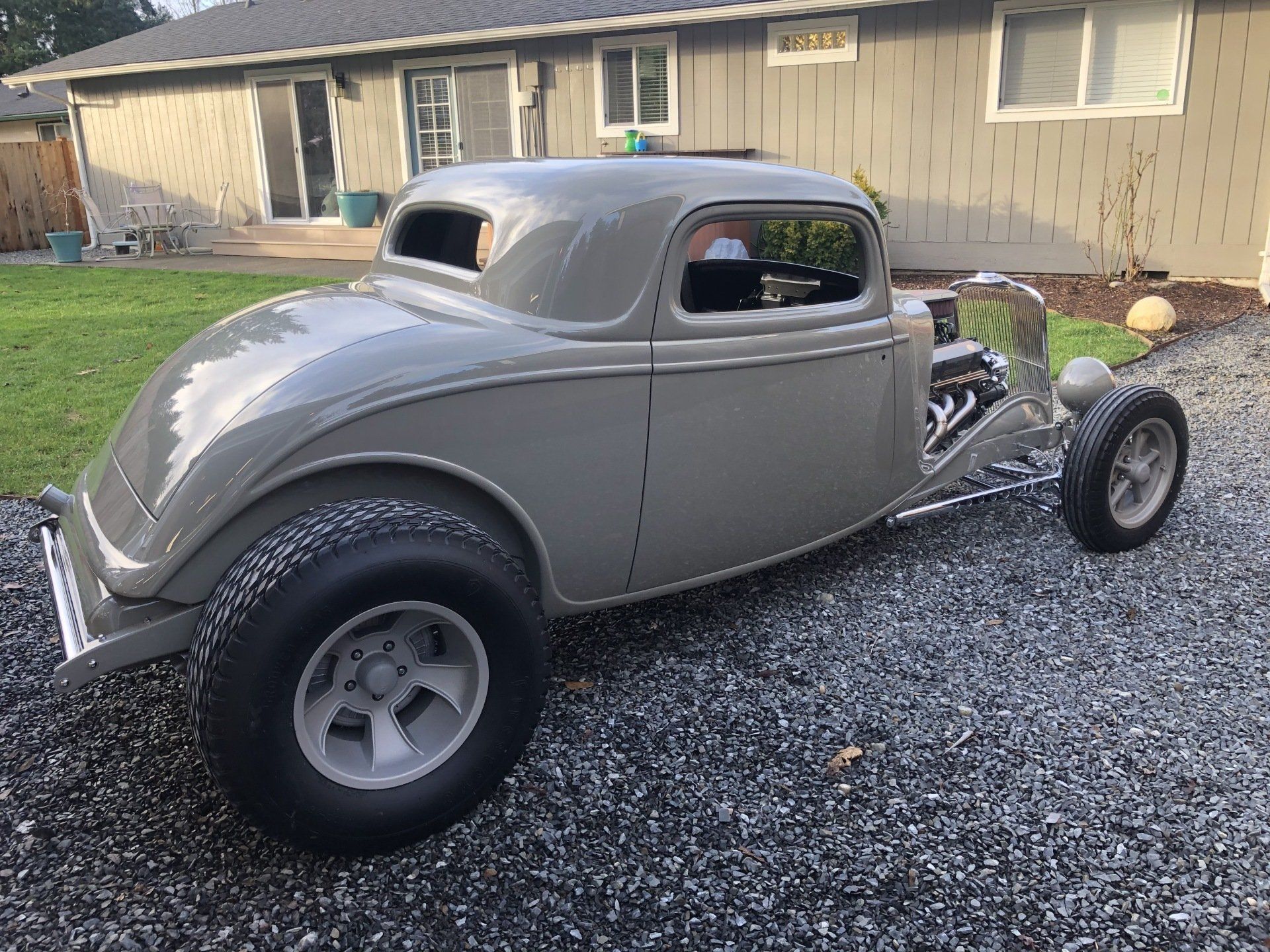 A gray hot rod is parked in front of a house.