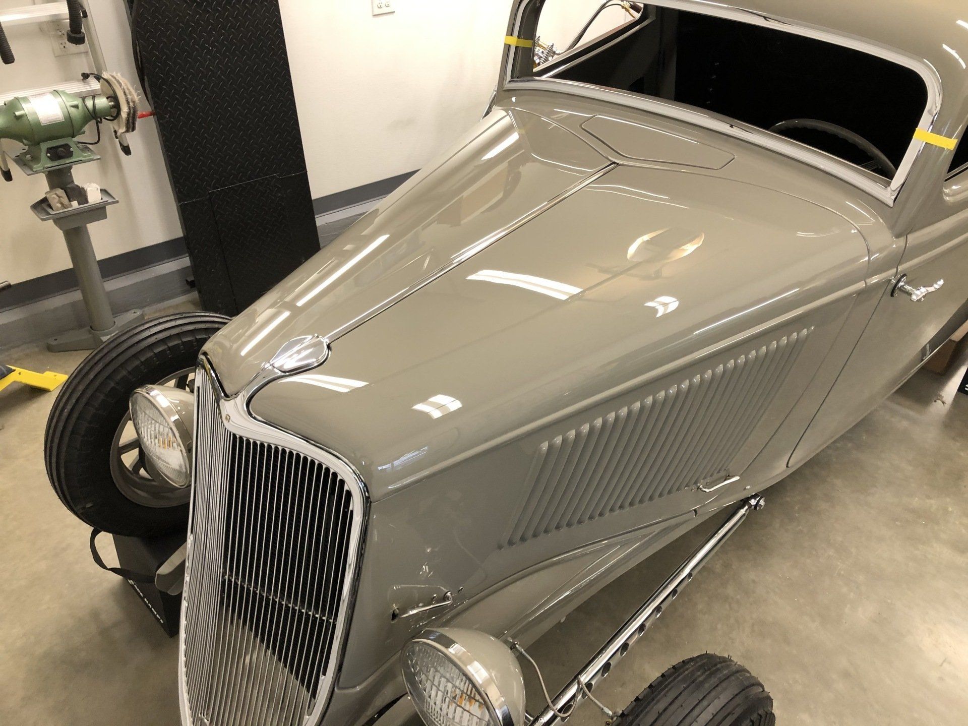 A gray car is parked in a garage next to a drill.