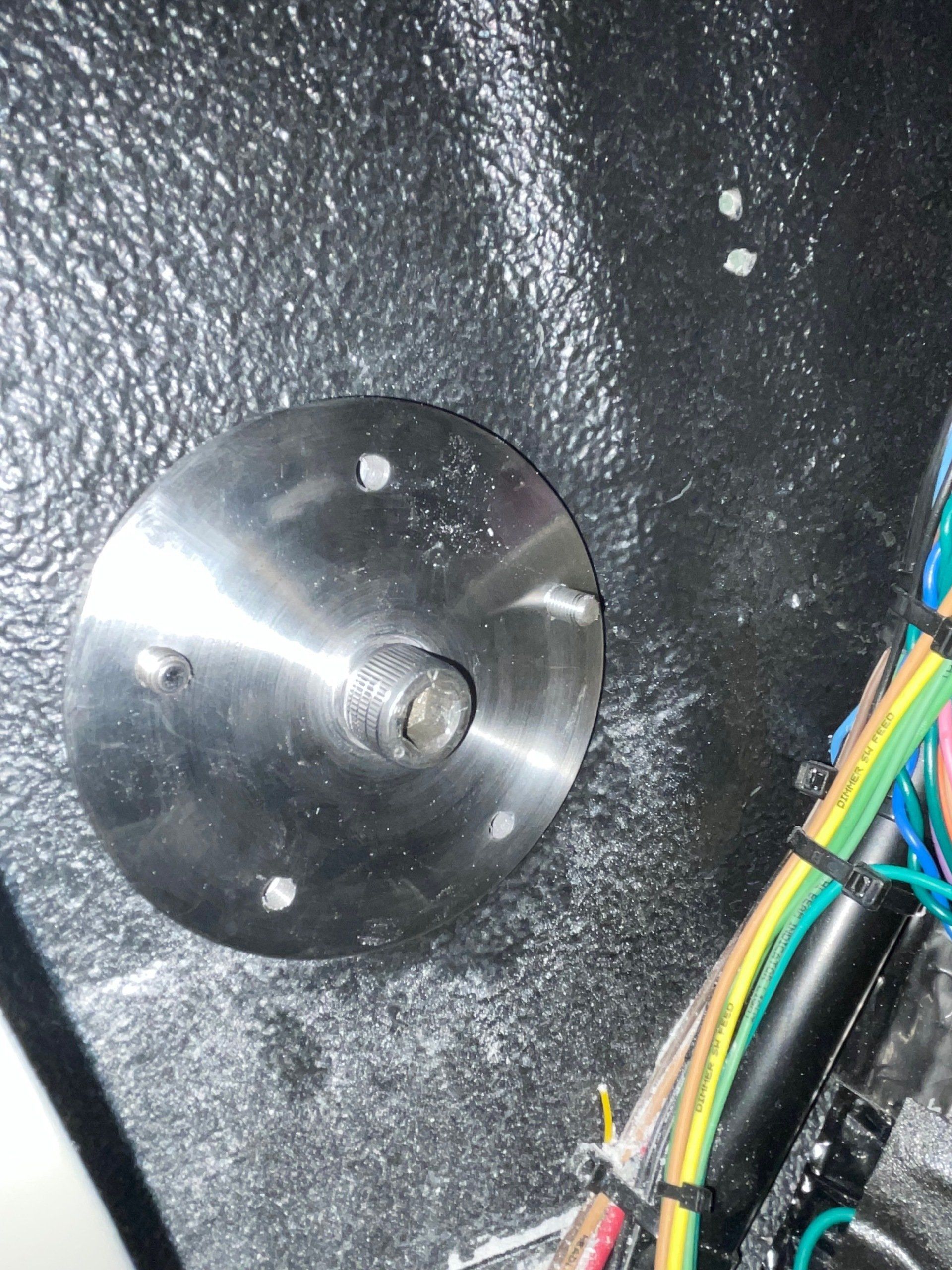 A metal plate with a screw in it is sitting on a black surface next to a bunch of wires.