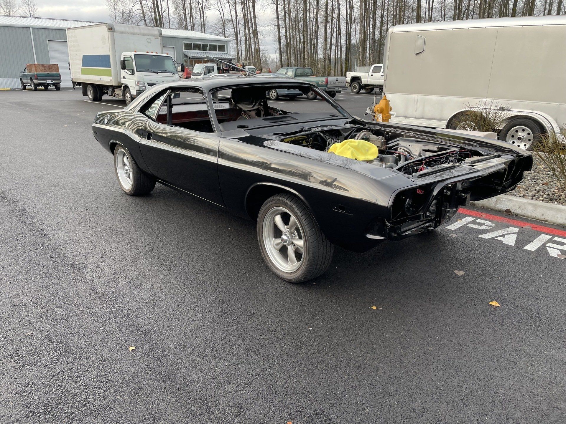 A black dodge challenger with the hood open is parked in a parking lot.