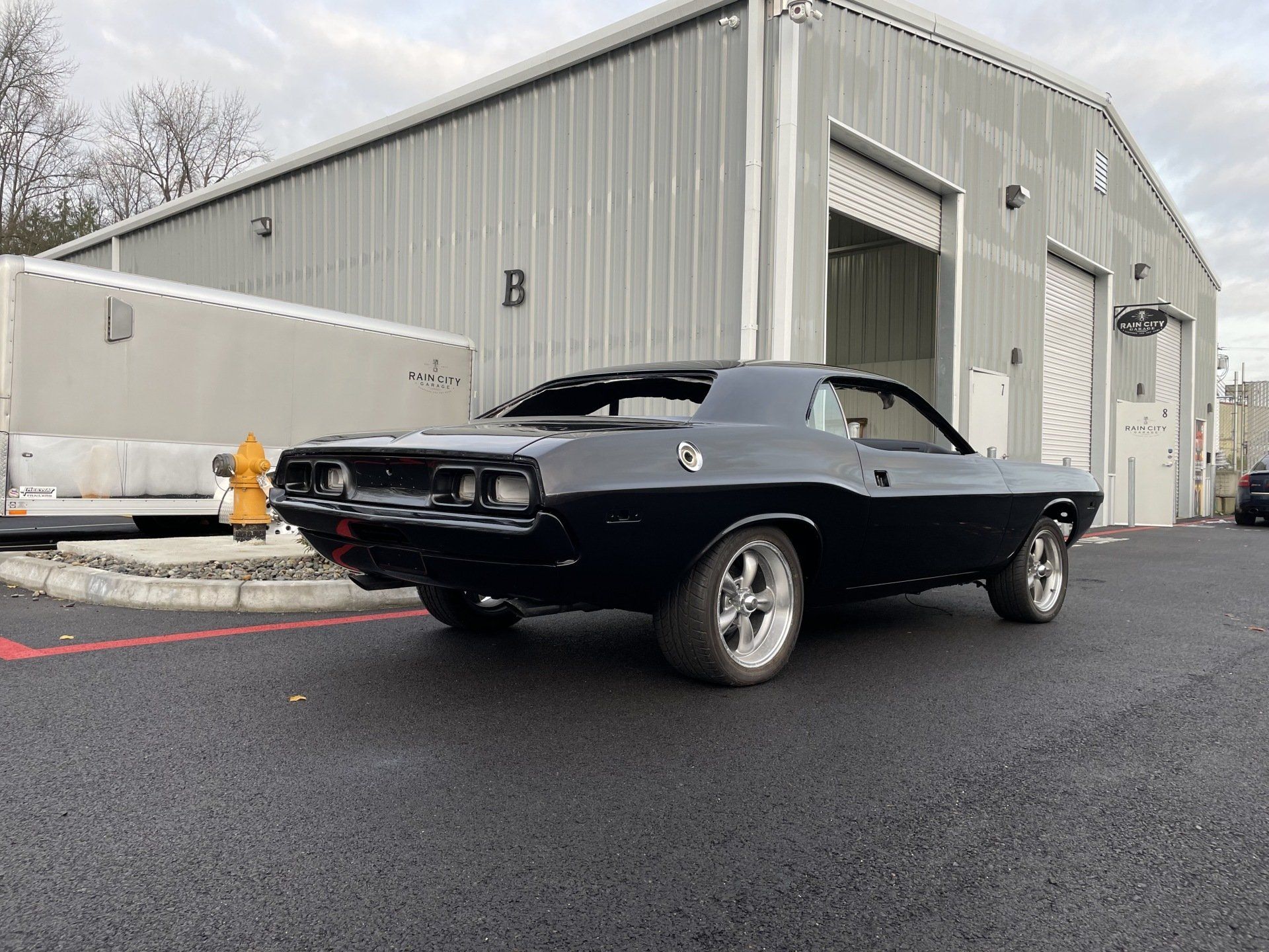 A black dodge challenger is parked in front of a garage.