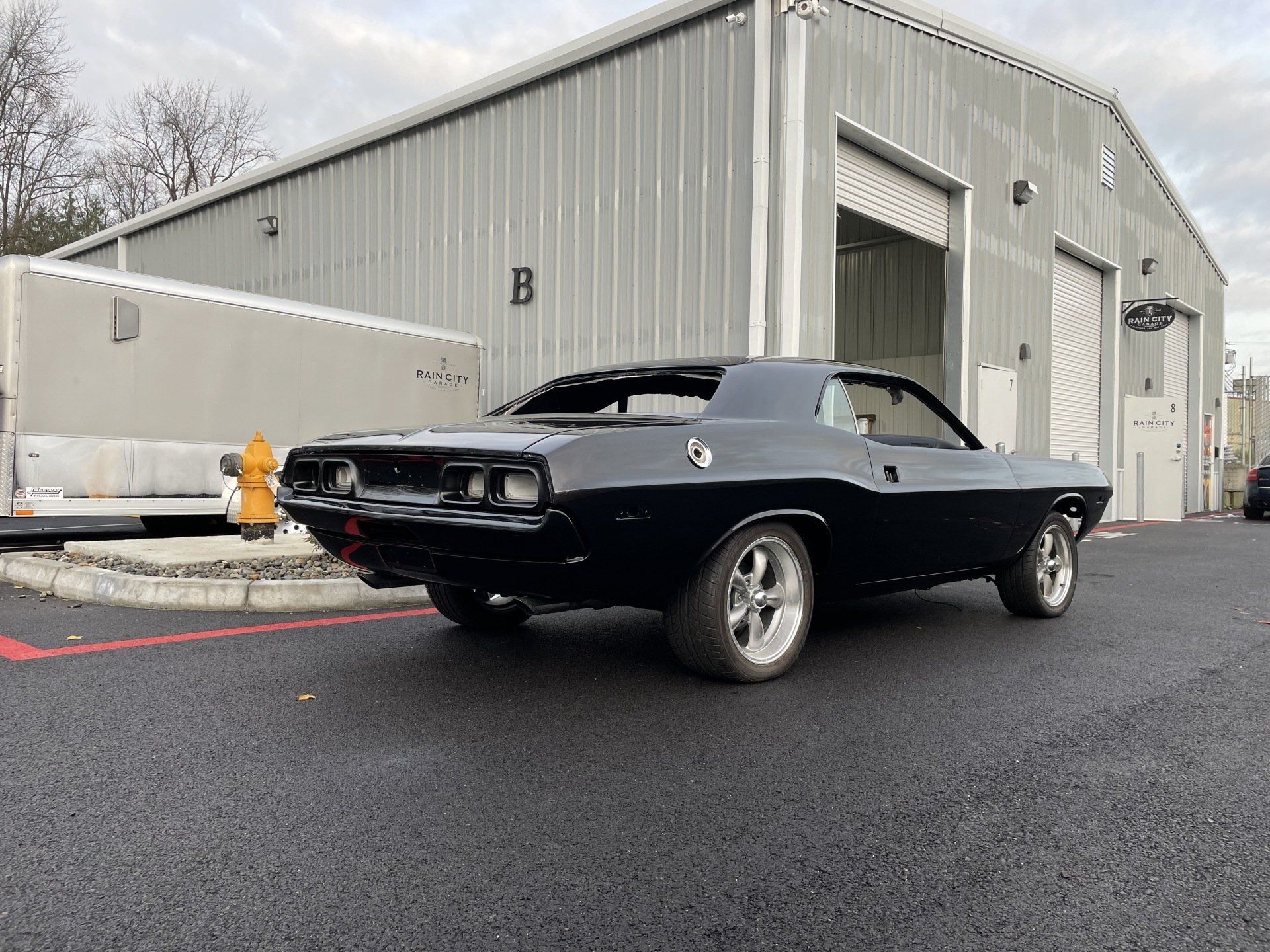 A black dodge challenger is parked in front of a garage.