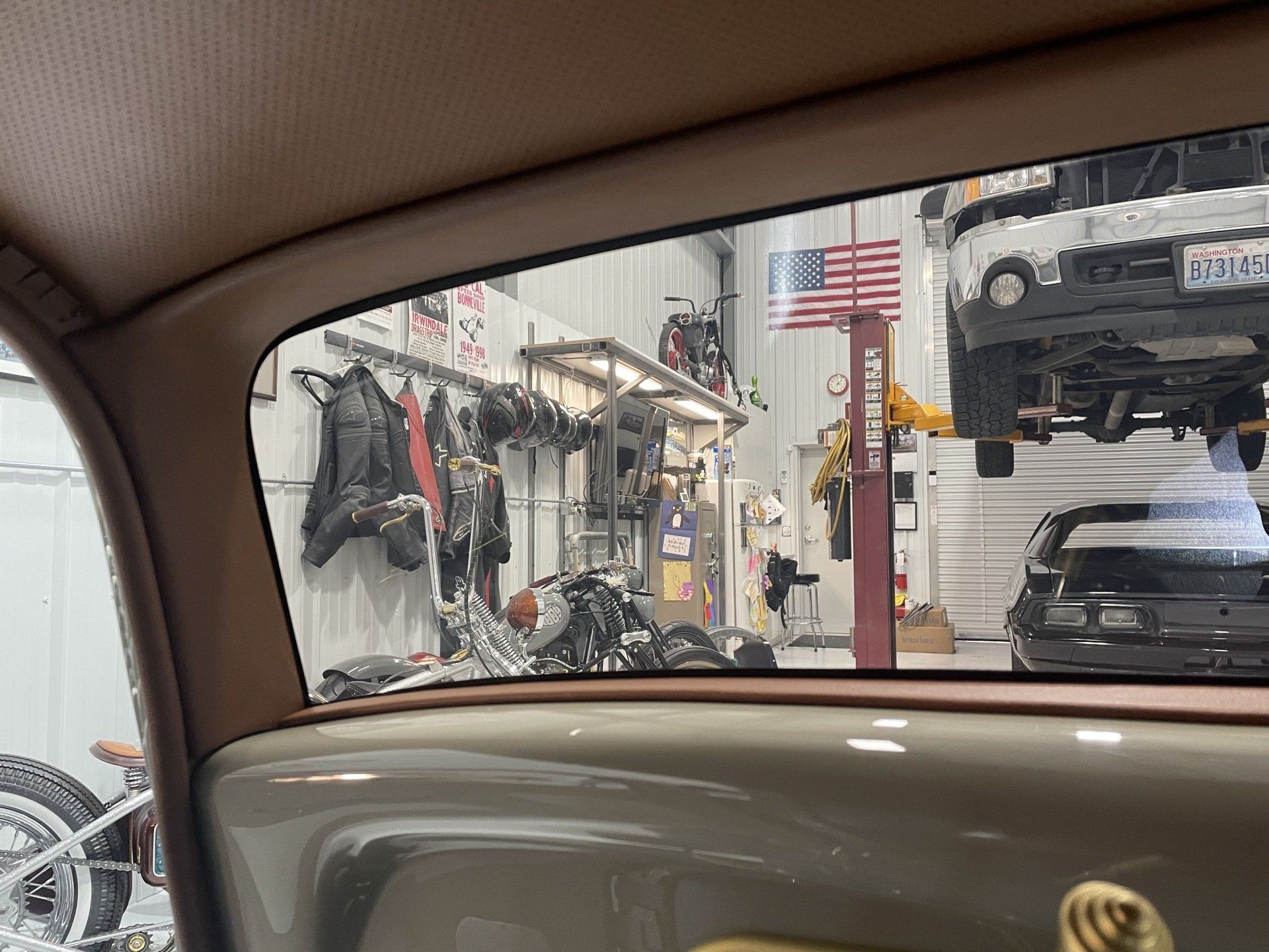 A car is parked in a garage with a motorcycle in the background.