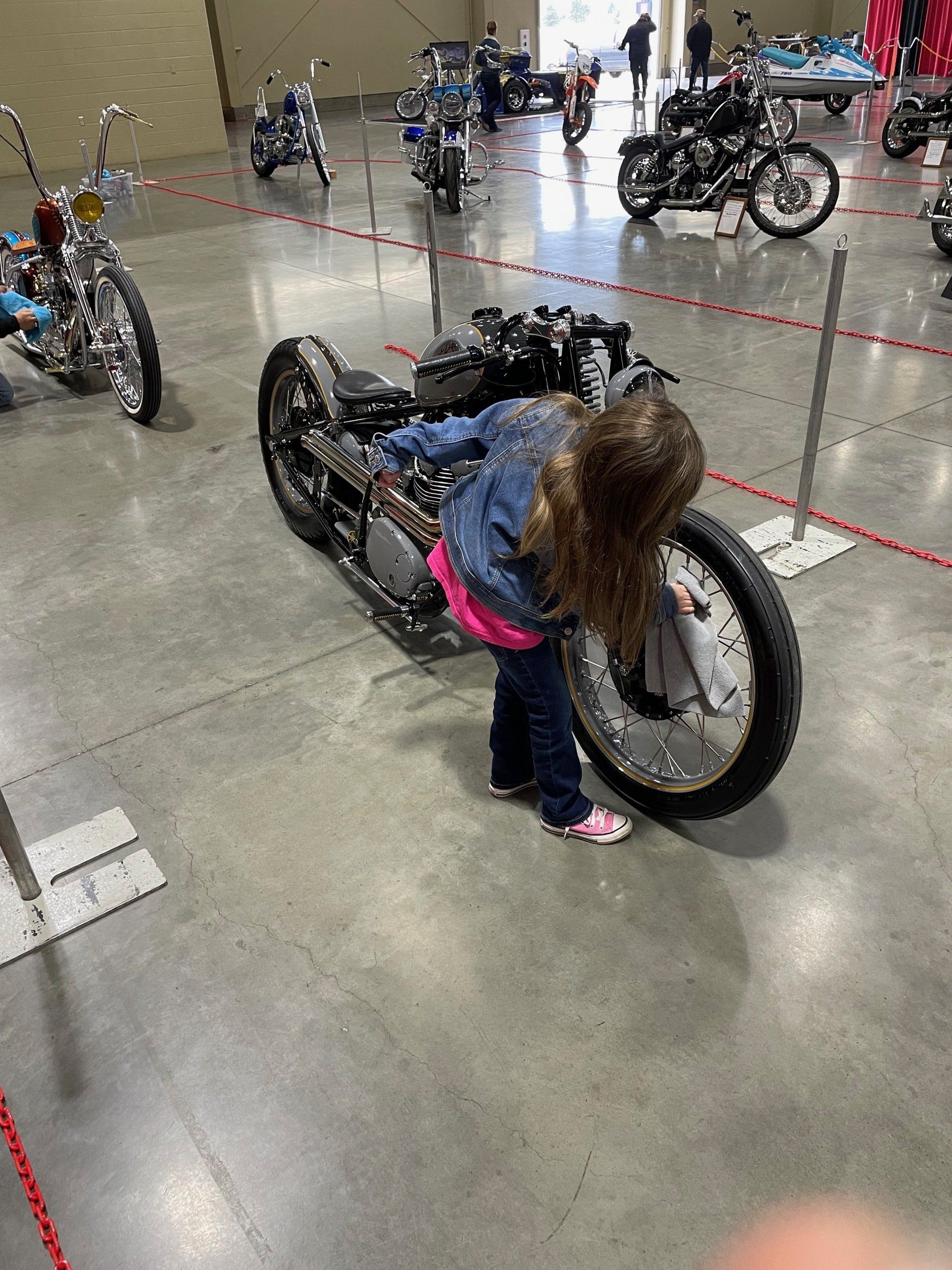 A little girl is looking at a motorcycle at a motorcycle show.