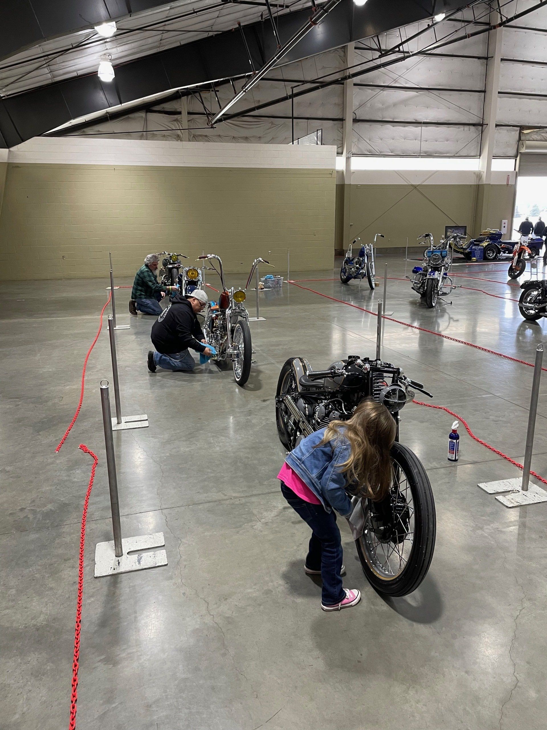 A little girl is looking at a motorcycle in a warehouse.