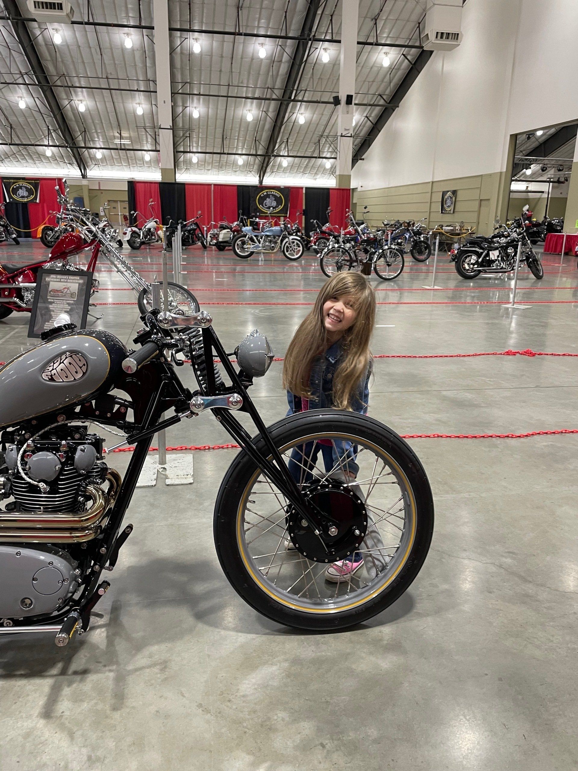 A little girl is standing next to a motorcycle in a warehouse.