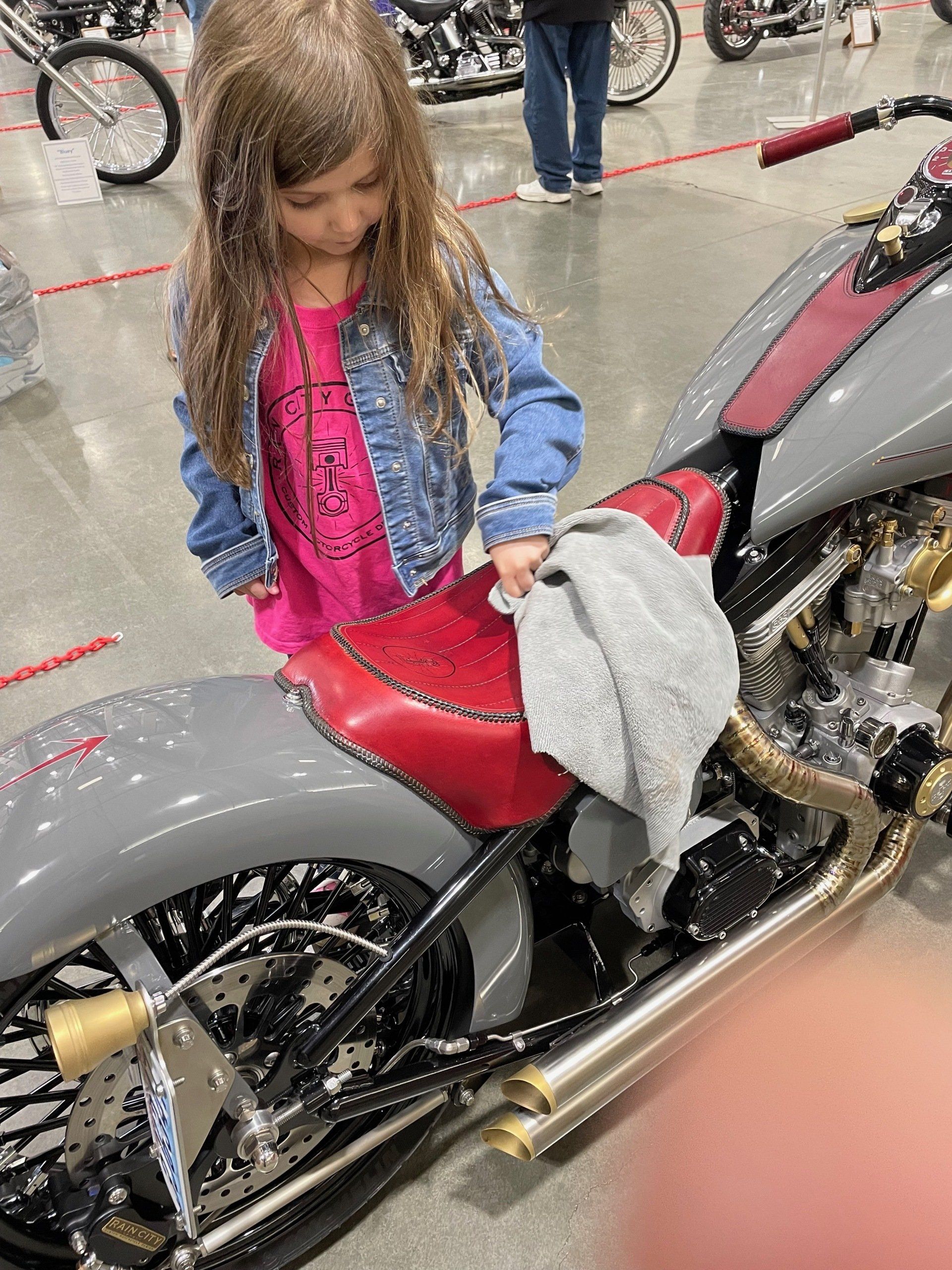 A little girl is cleaning a motorcycle seat with a towel.