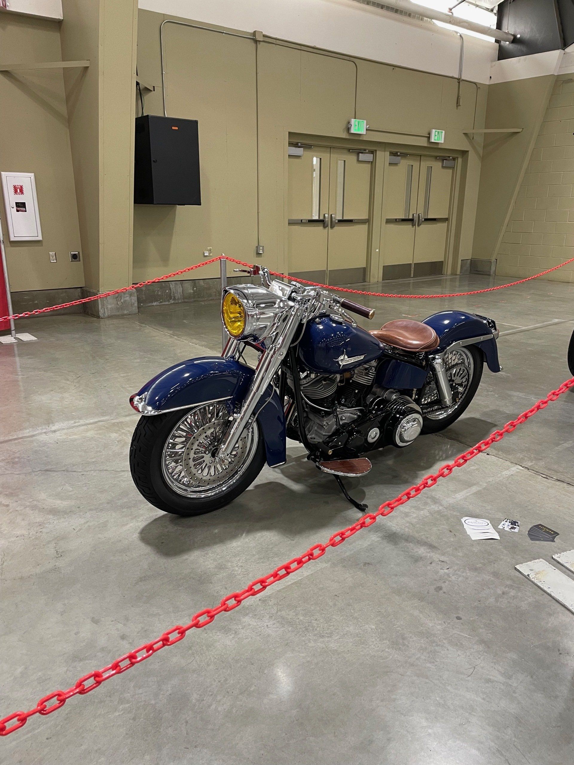 A blue motorcycle is parked in a room behind a chain link fence.