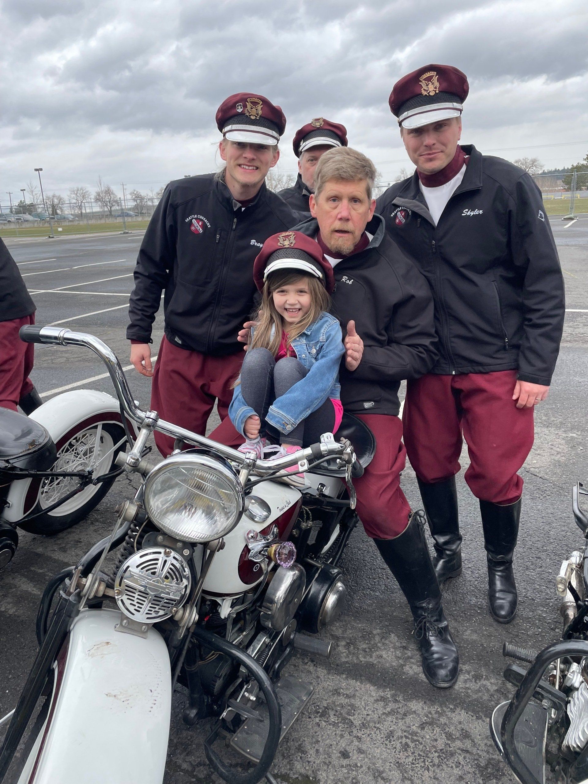 A group of men are posing for a picture with a little girl on a motorcycle.