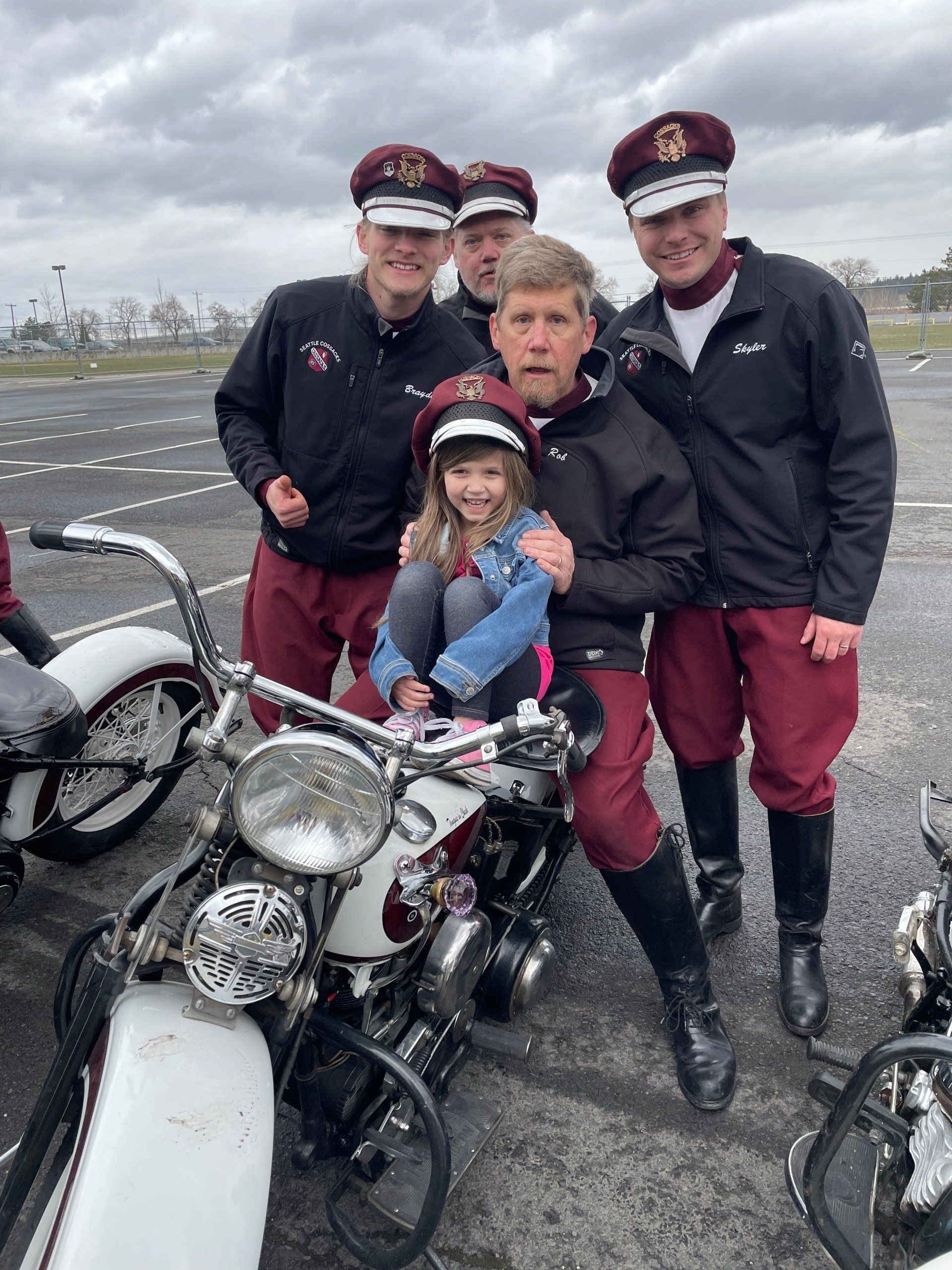 A group of men are posing for a picture with a little girl sitting on a motorcycle.