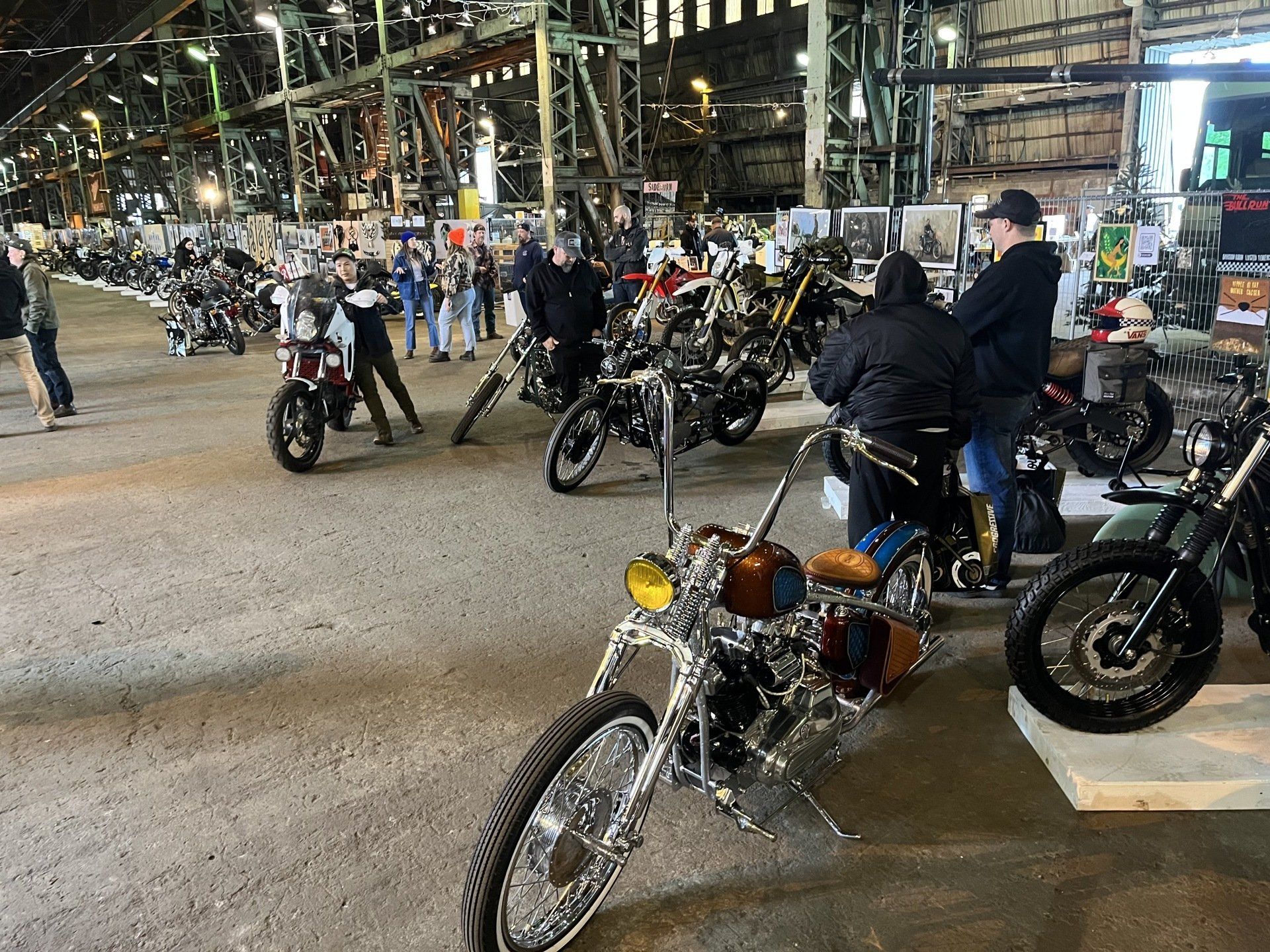 A group of people are standing around motorcycles in a warehouse.