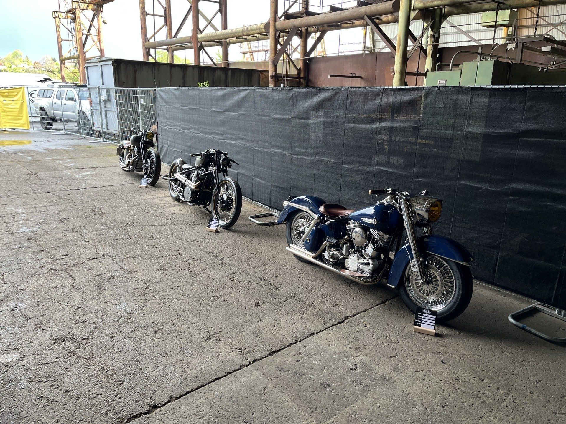 Three motorcycles are parked in front of a fence.