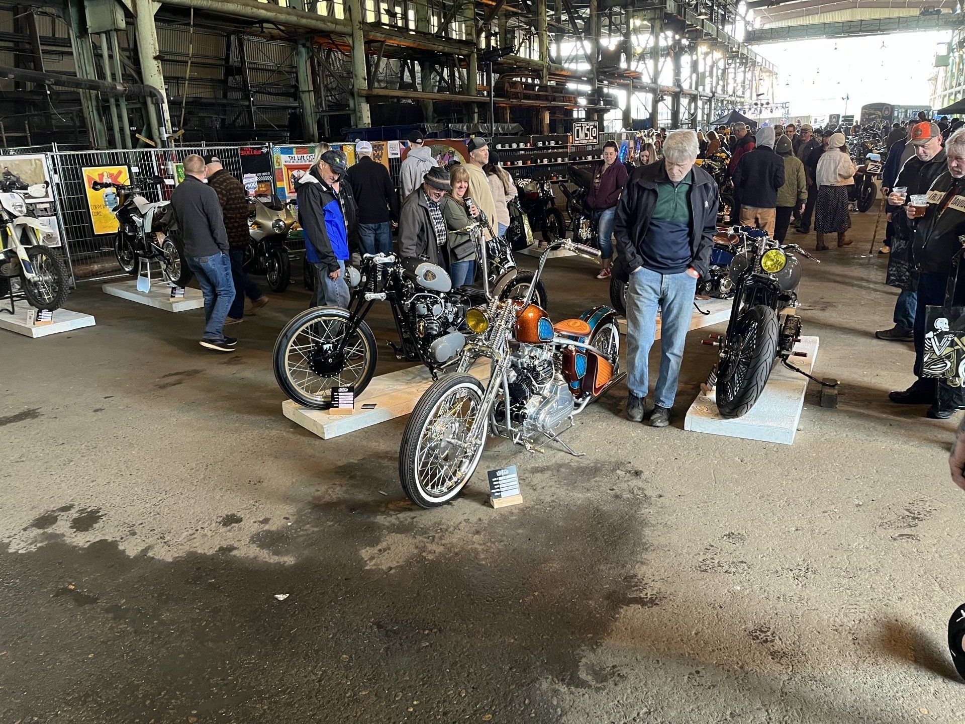 A group of people are standing around motorcycles in a warehouse.