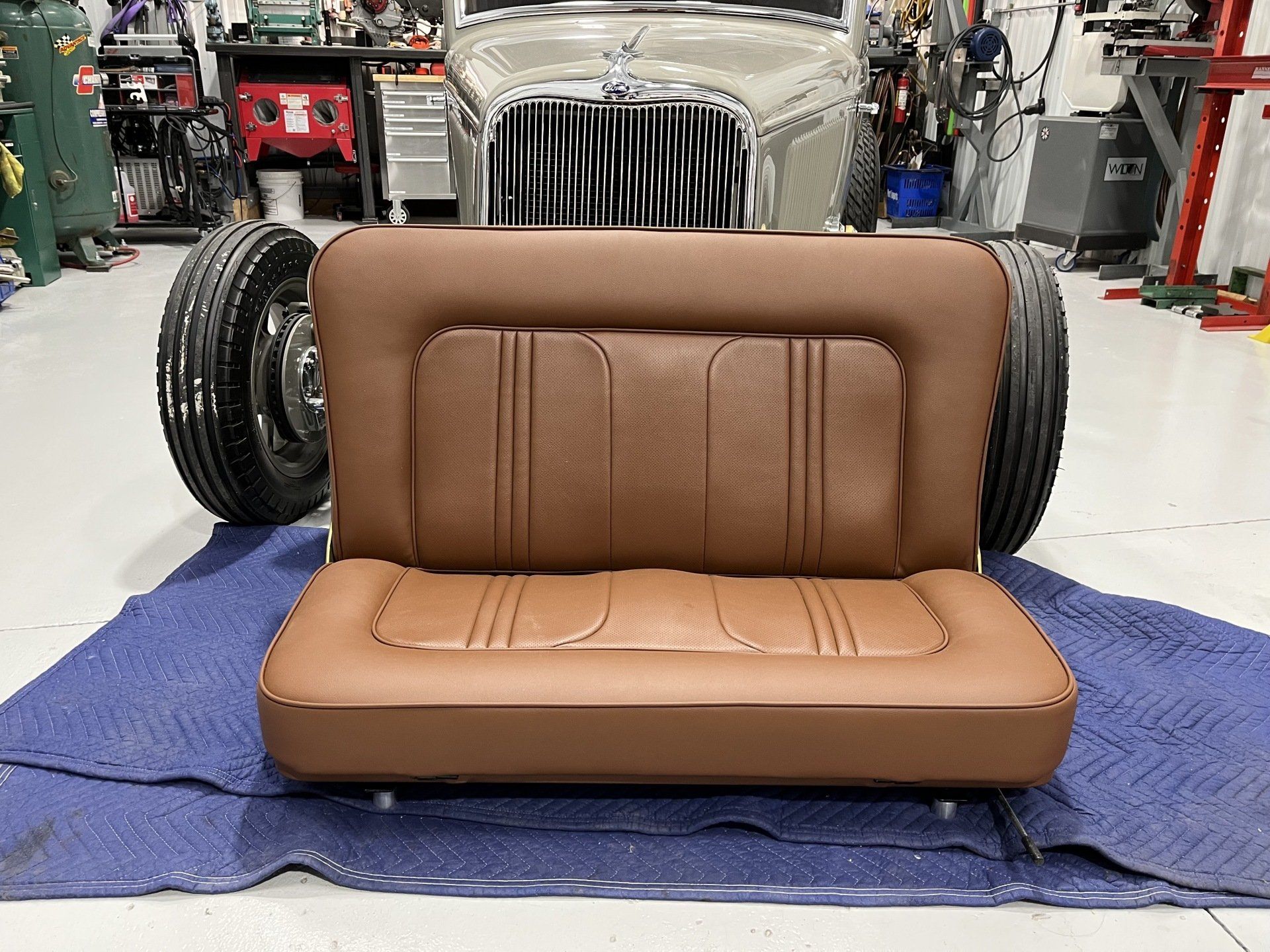 A brown couch is sitting in front of a car in a garage.