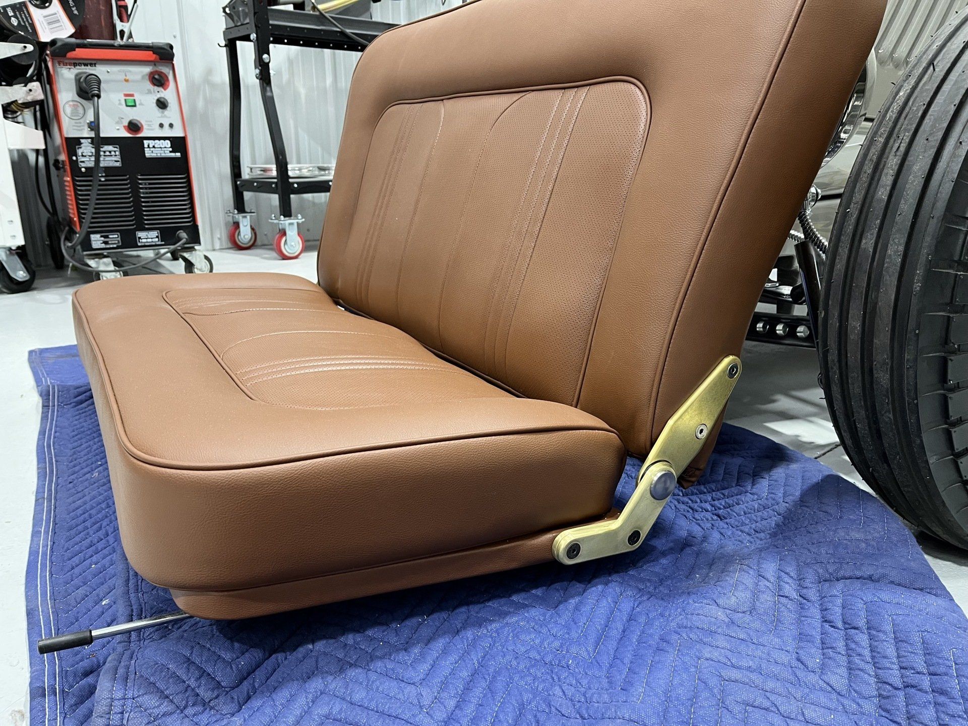 A brown leather seat is sitting on a blue mat next to a tire.