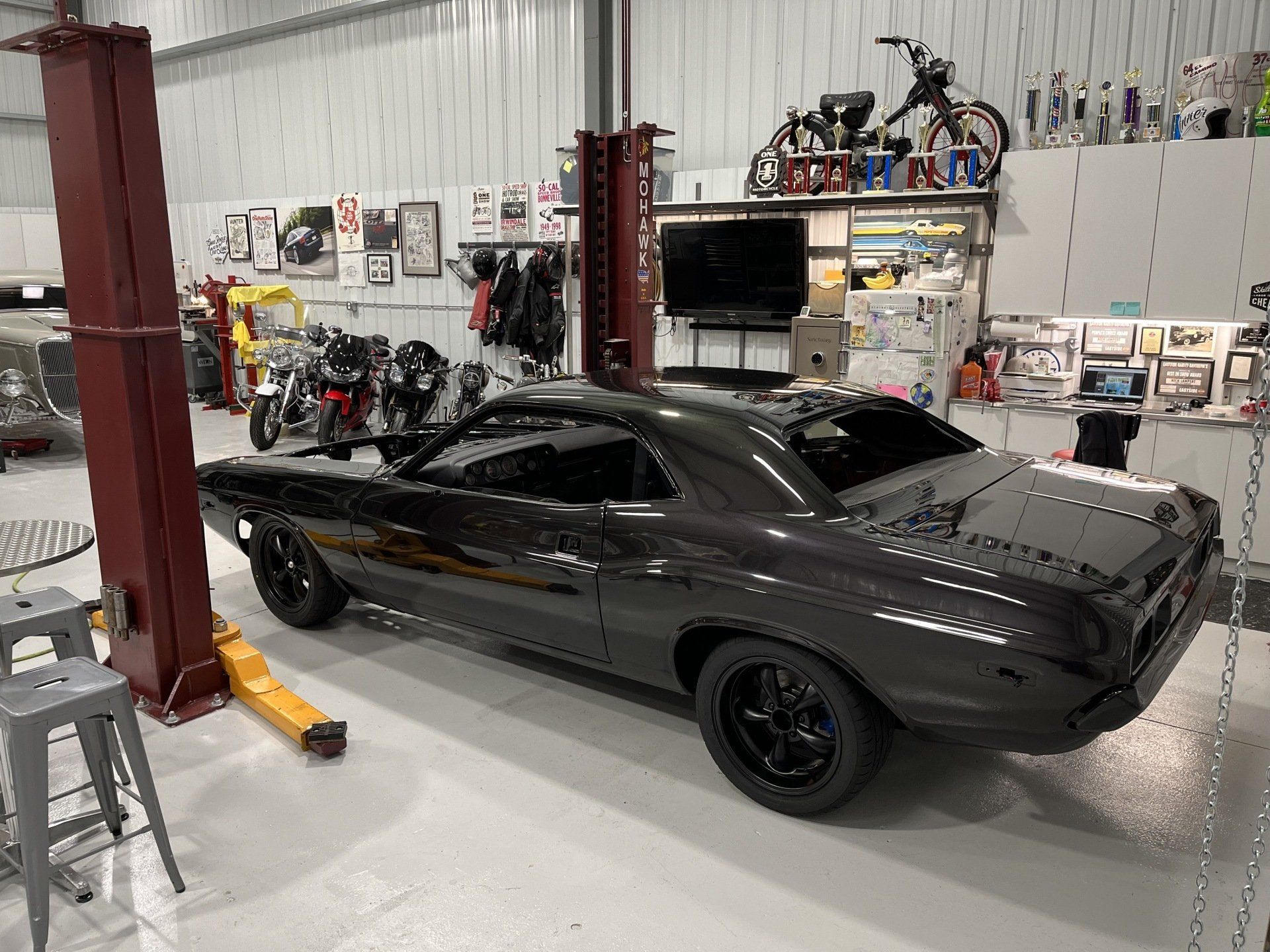 A black dodge challenger is parked on a lift in a garage.