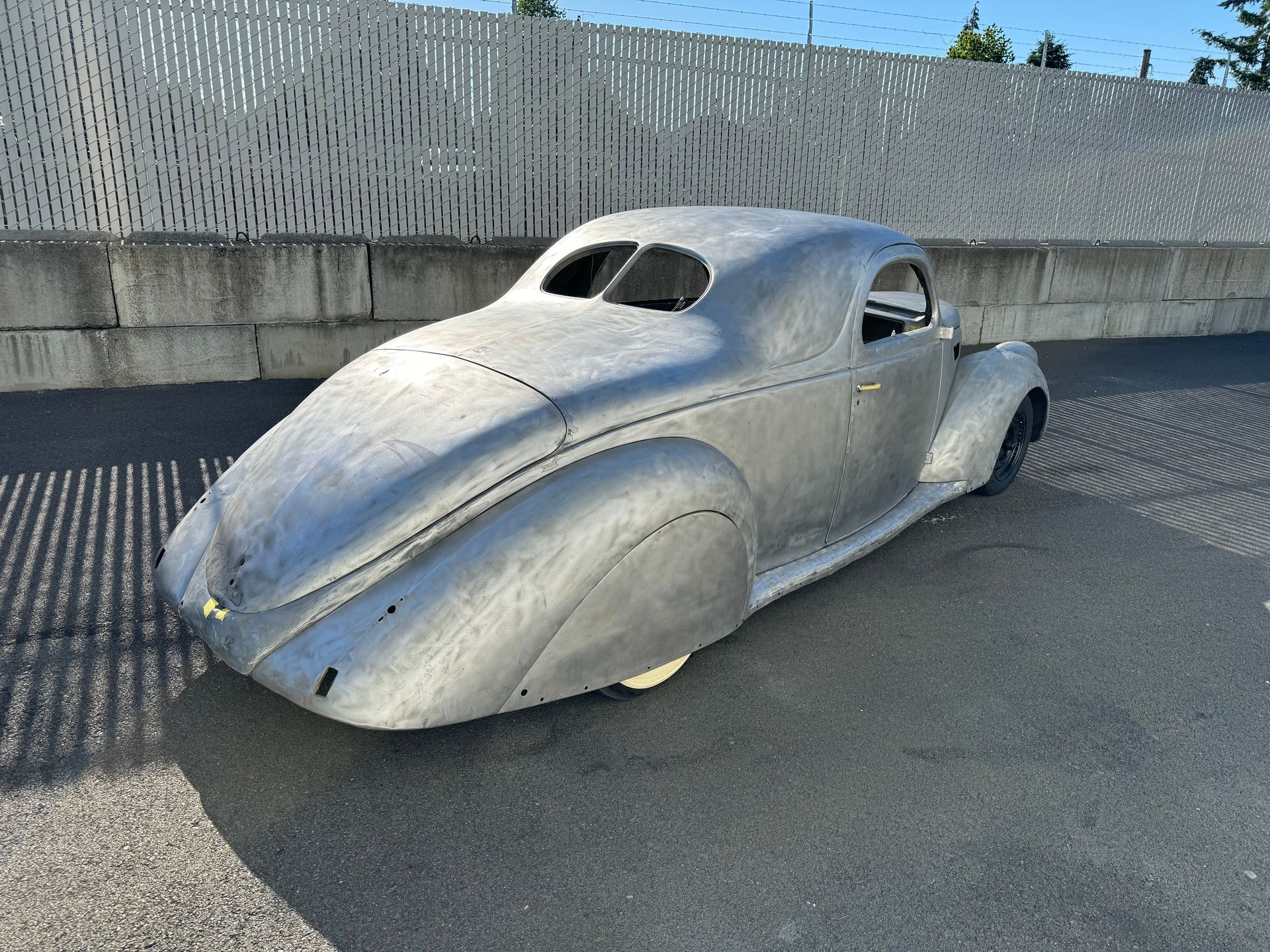A silver car is parked in front of a white fence.