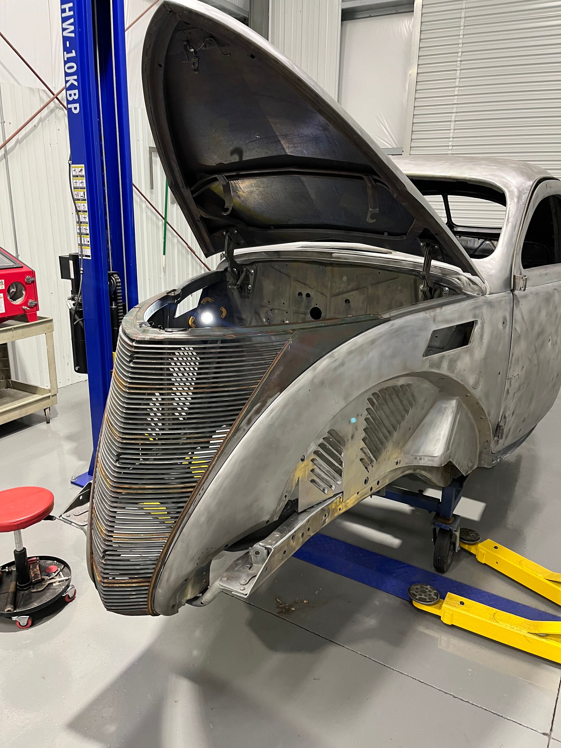 A car with the hood open is sitting on a lift in a garage.