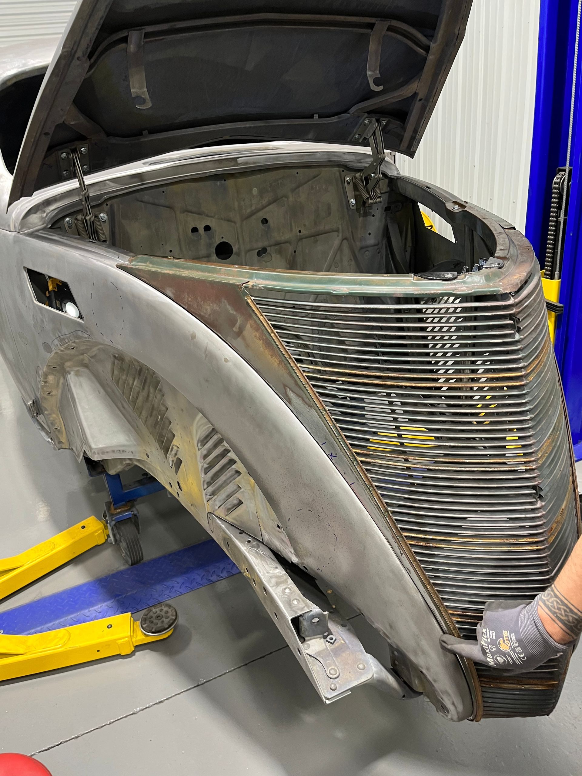 A car with the hood open is sitting on a lift in a garage.