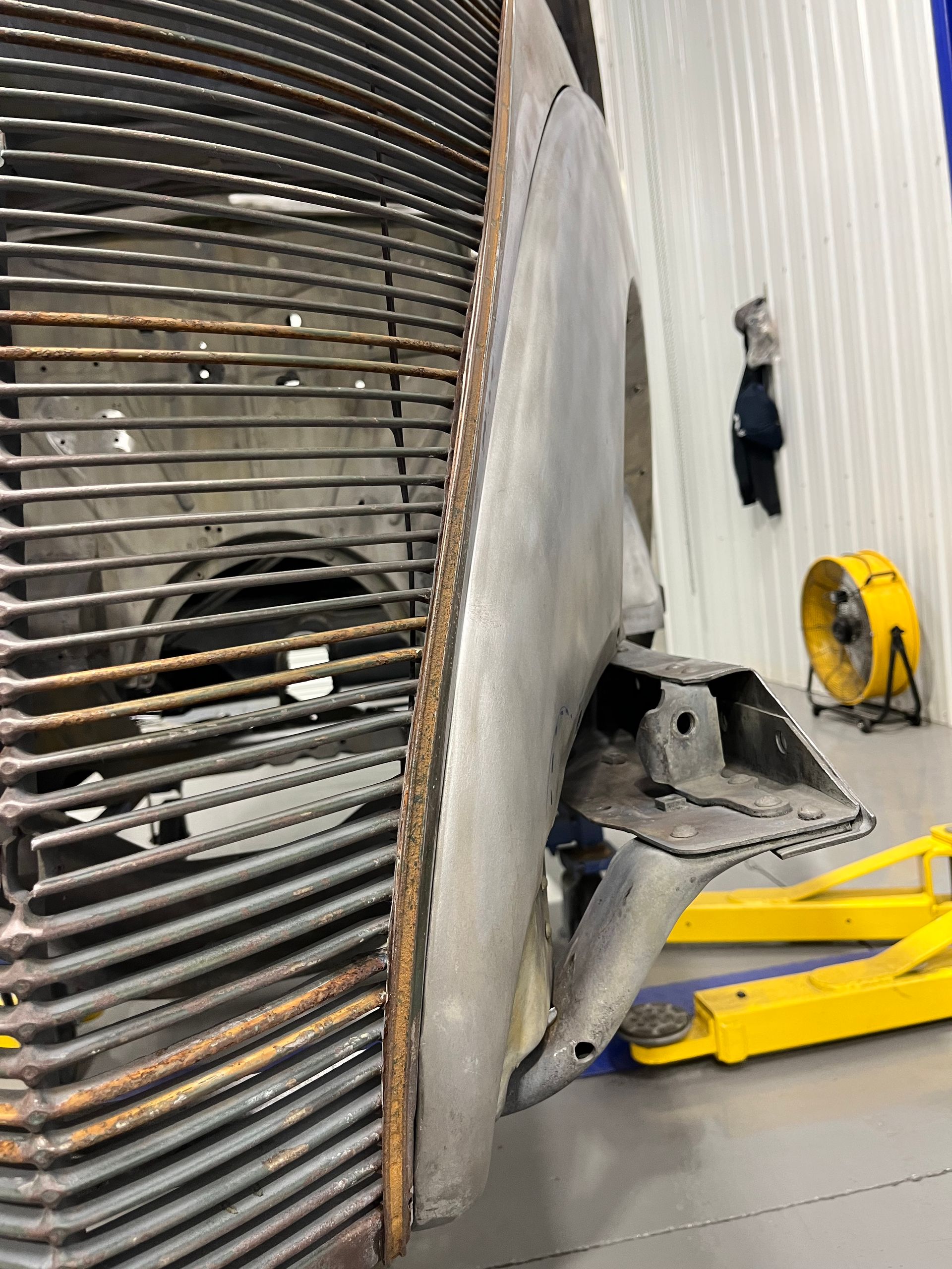 A car is sitting on a lift in a garage next to a yellow fan.