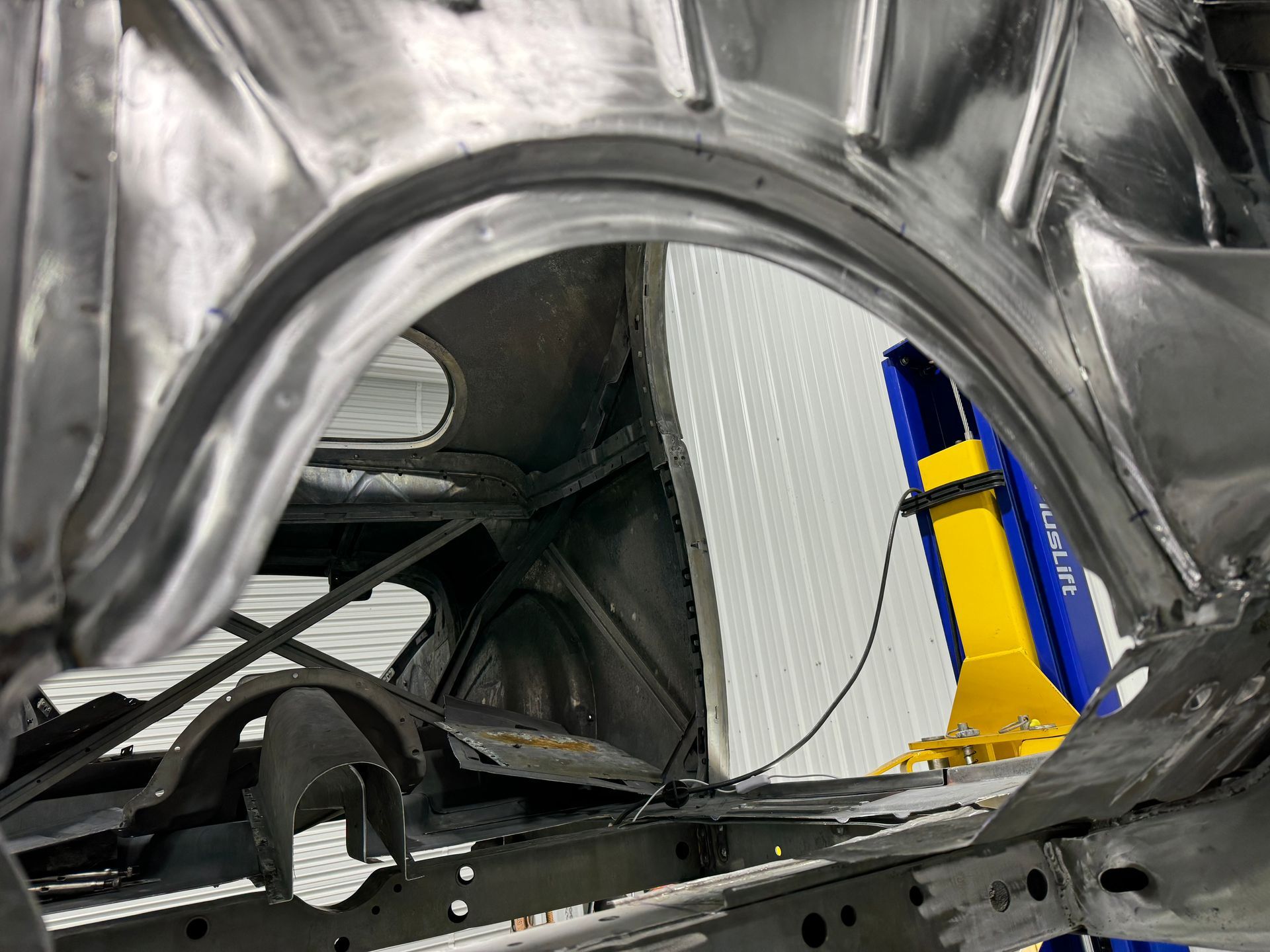 A car is being built in a garage with a blue and yellow lift.