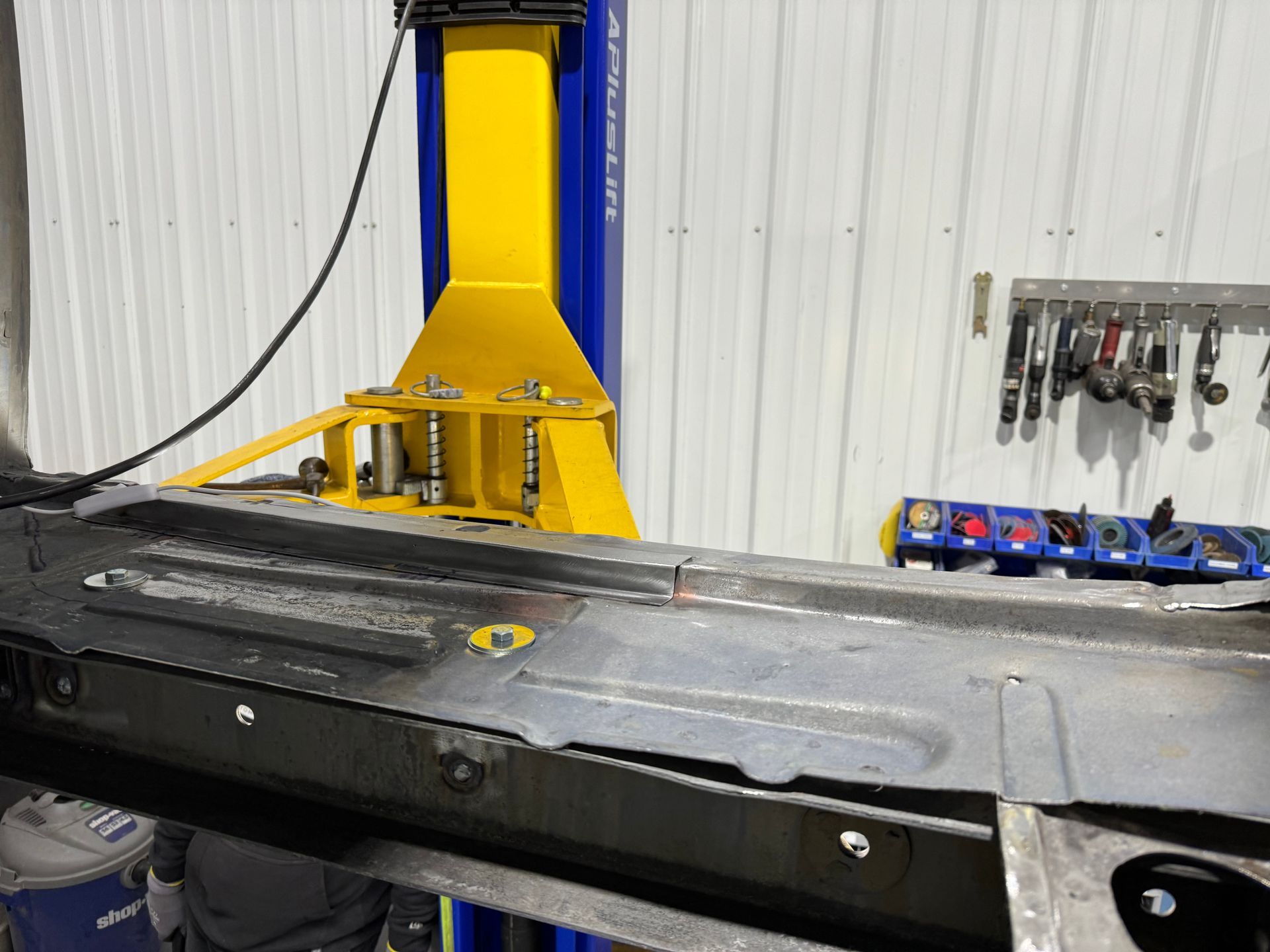 A yellow and blue lift is sitting next to a piece of metal in a garage.