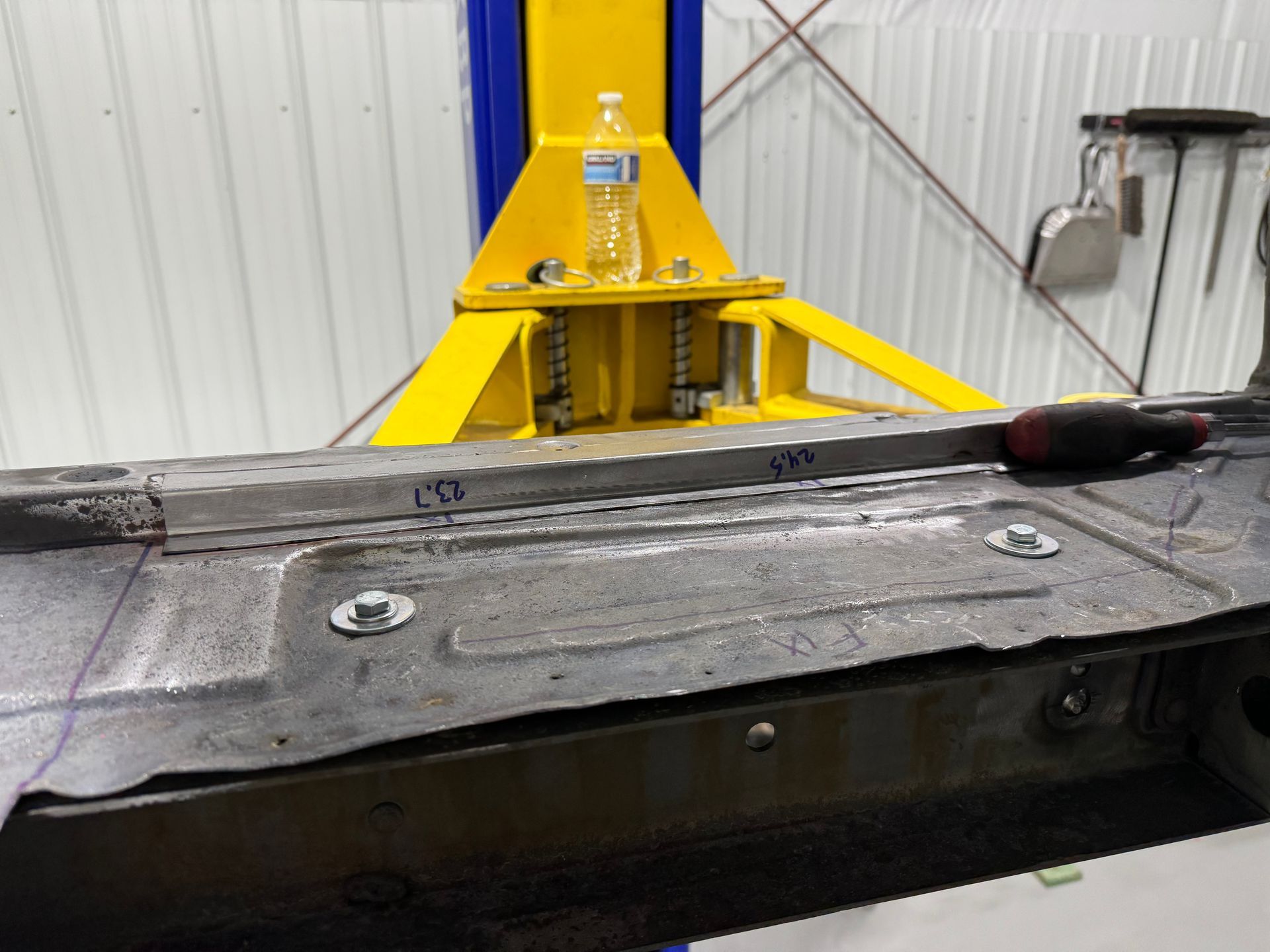 A screwdriver is sitting on a piece of metal next to a yellow lift.