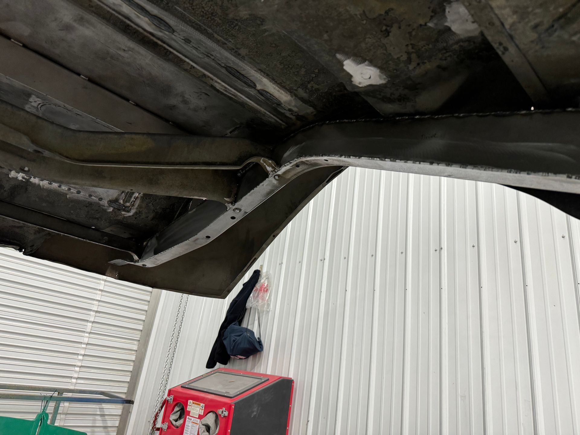 A person is standing under a car in front of a white building.