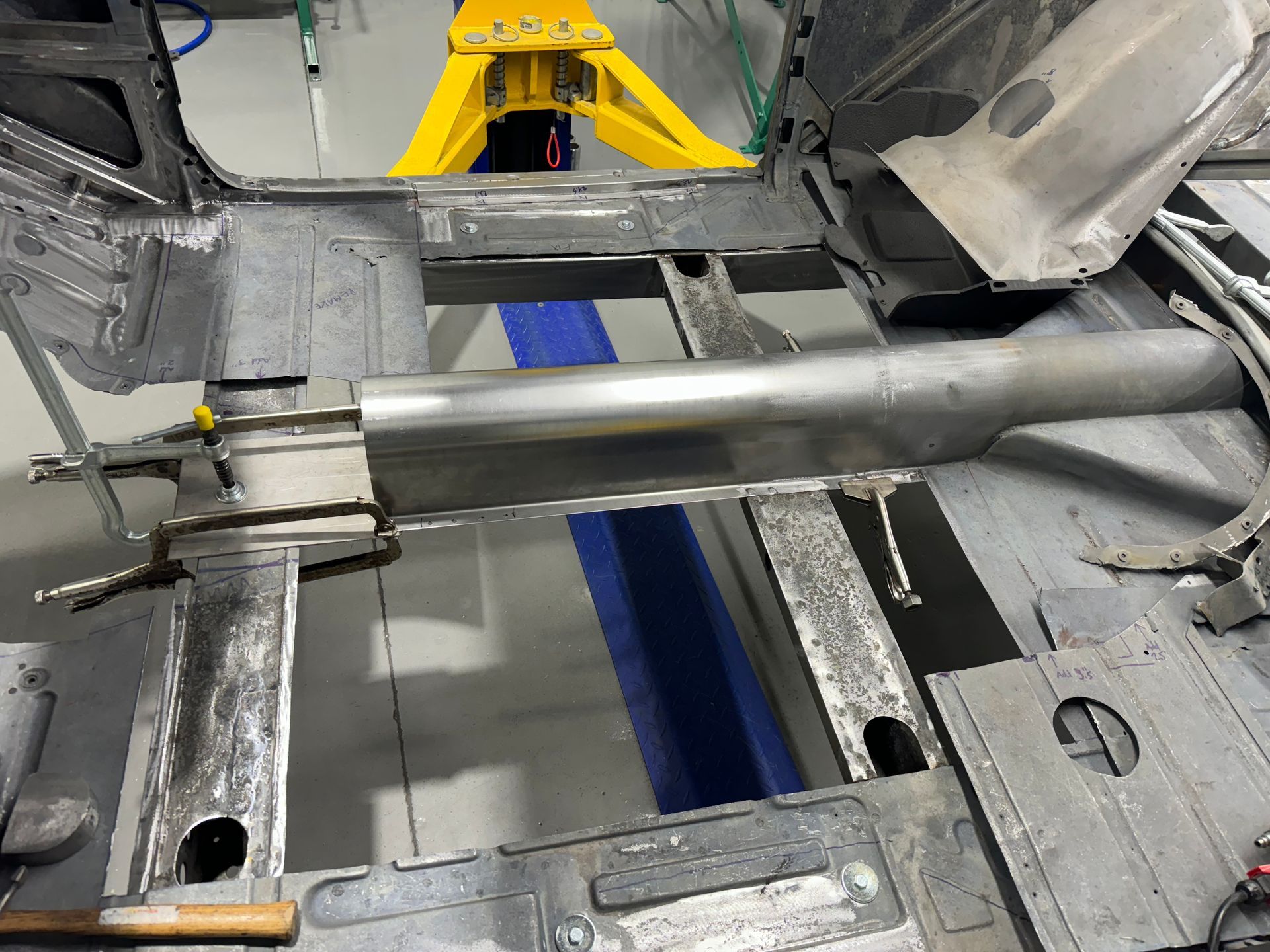 A car is being built in a garage with a yellow forklift in the background.