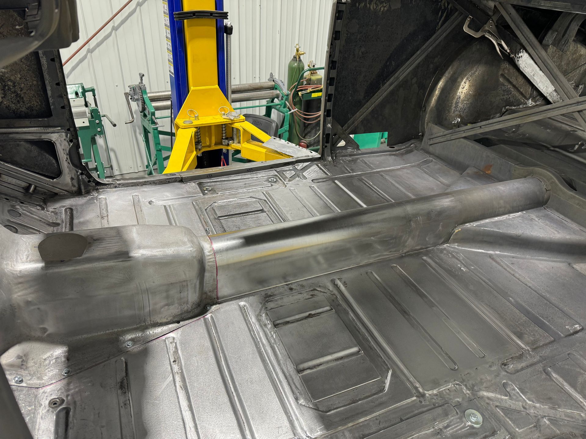 A car is being built in a garage with a yellow crane in the background.