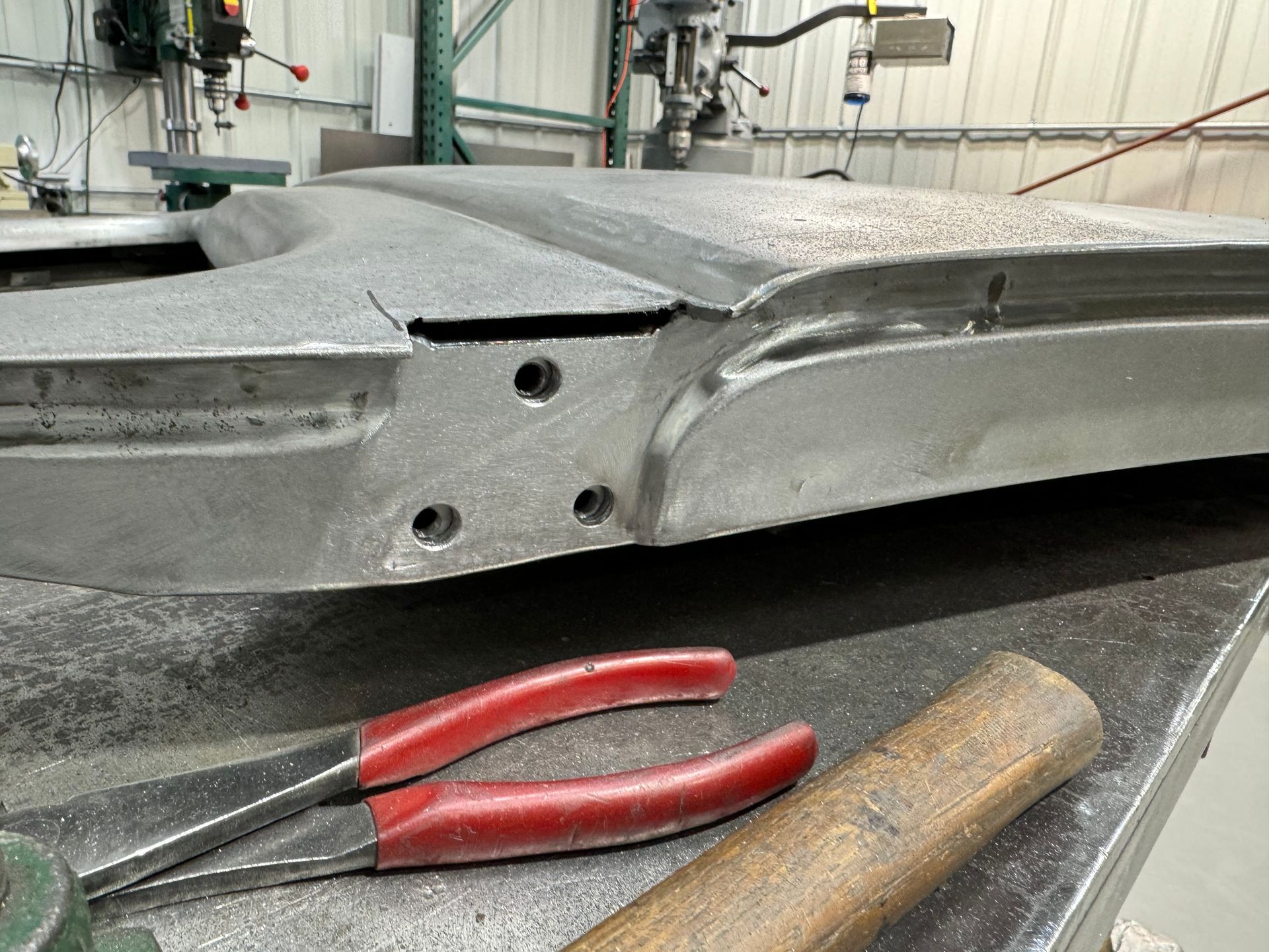 A pair of pliers and a hammer are on a table next to a piece of metal.