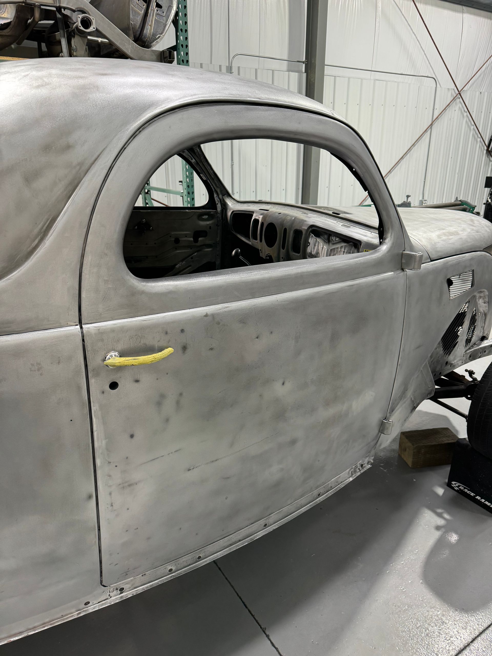 A silver car is sitting in a garage with a yellow handle on the door.