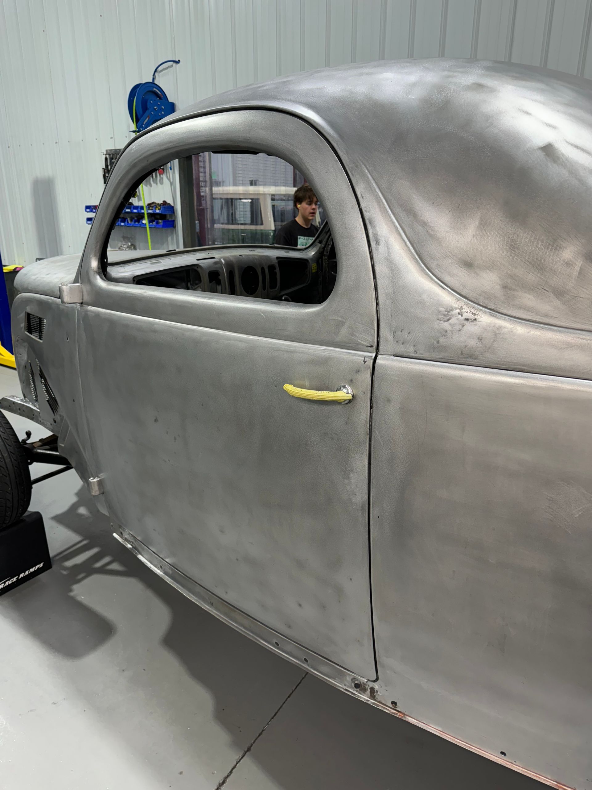 A man is standing next to a silver car in a garage.