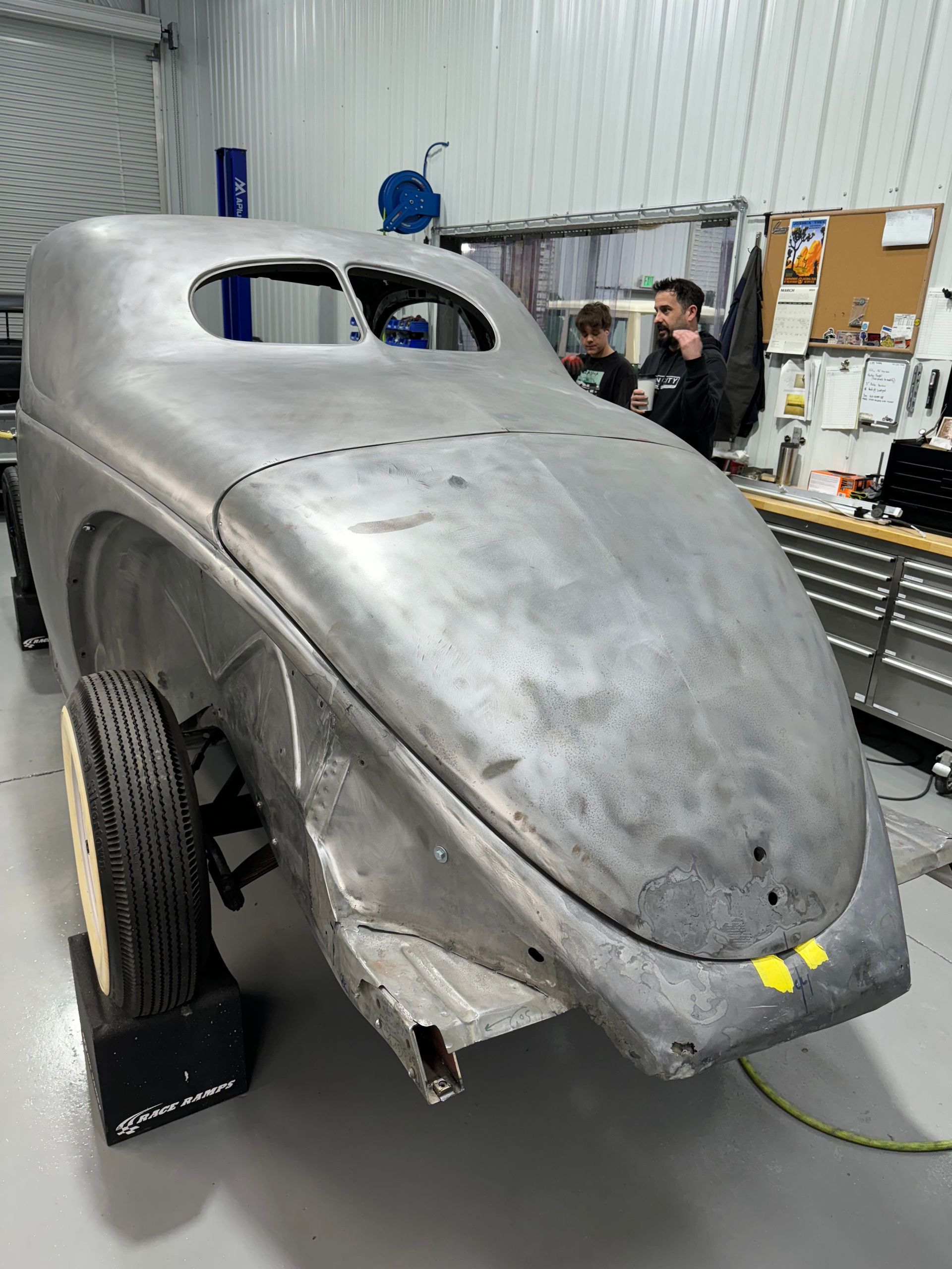 A silver car is being built in a garage.