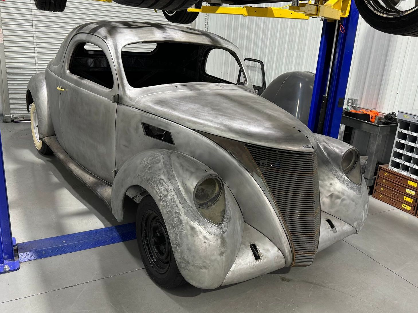 A silver car is sitting on a lift in a garage.