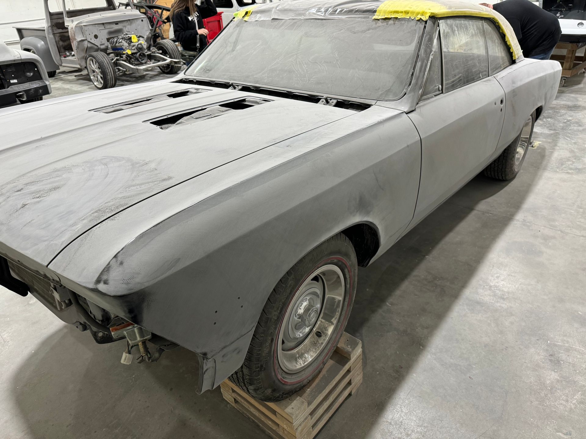 A gray car is sitting on a wooden pallet in a garage.