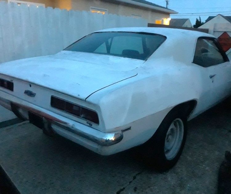 A white car is parked in front of a white fence